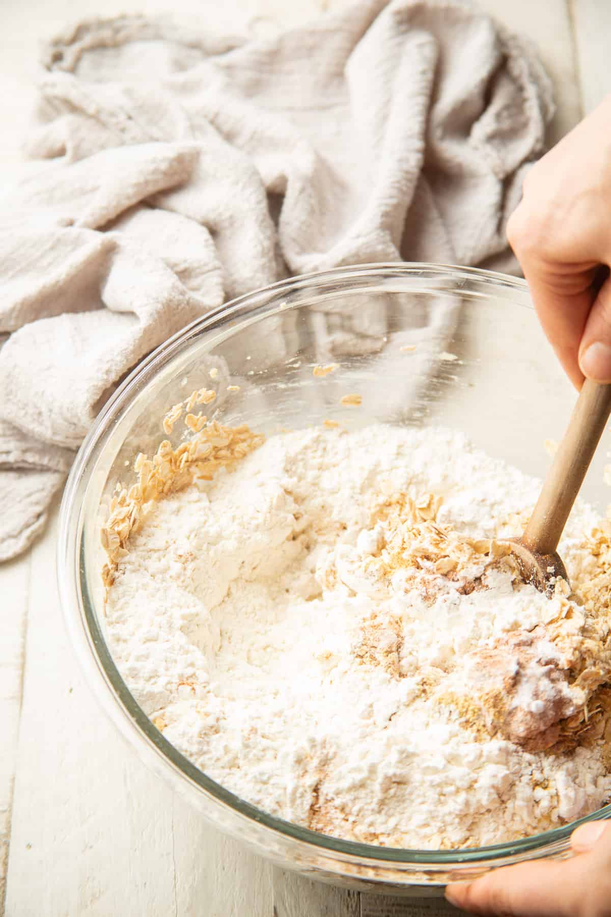 Hands stirring flour into a bowl of cookie dough.
