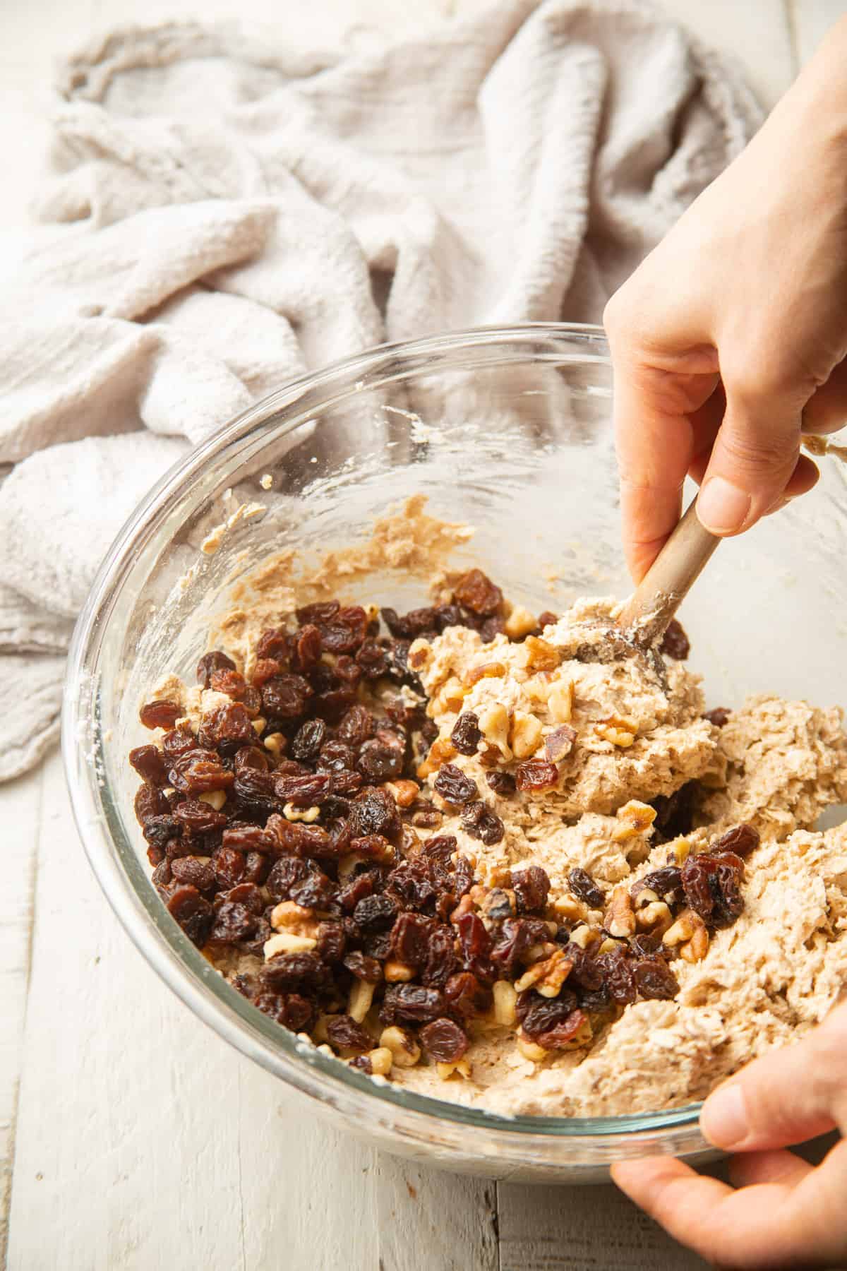 Hand stirring raisins and walnuts into a bowl of cookie dough.