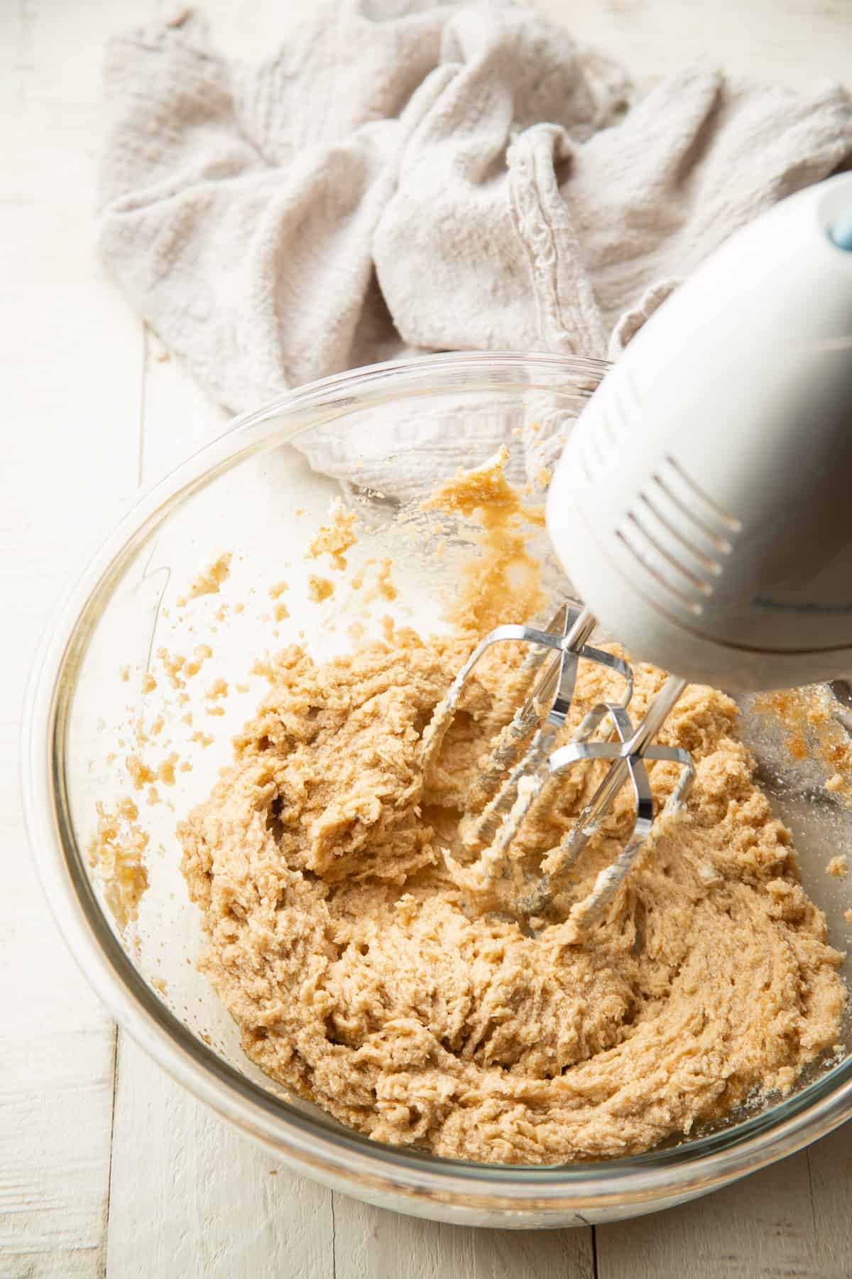 Electric mixer beating vegan butter and sugar together in a large bowl.