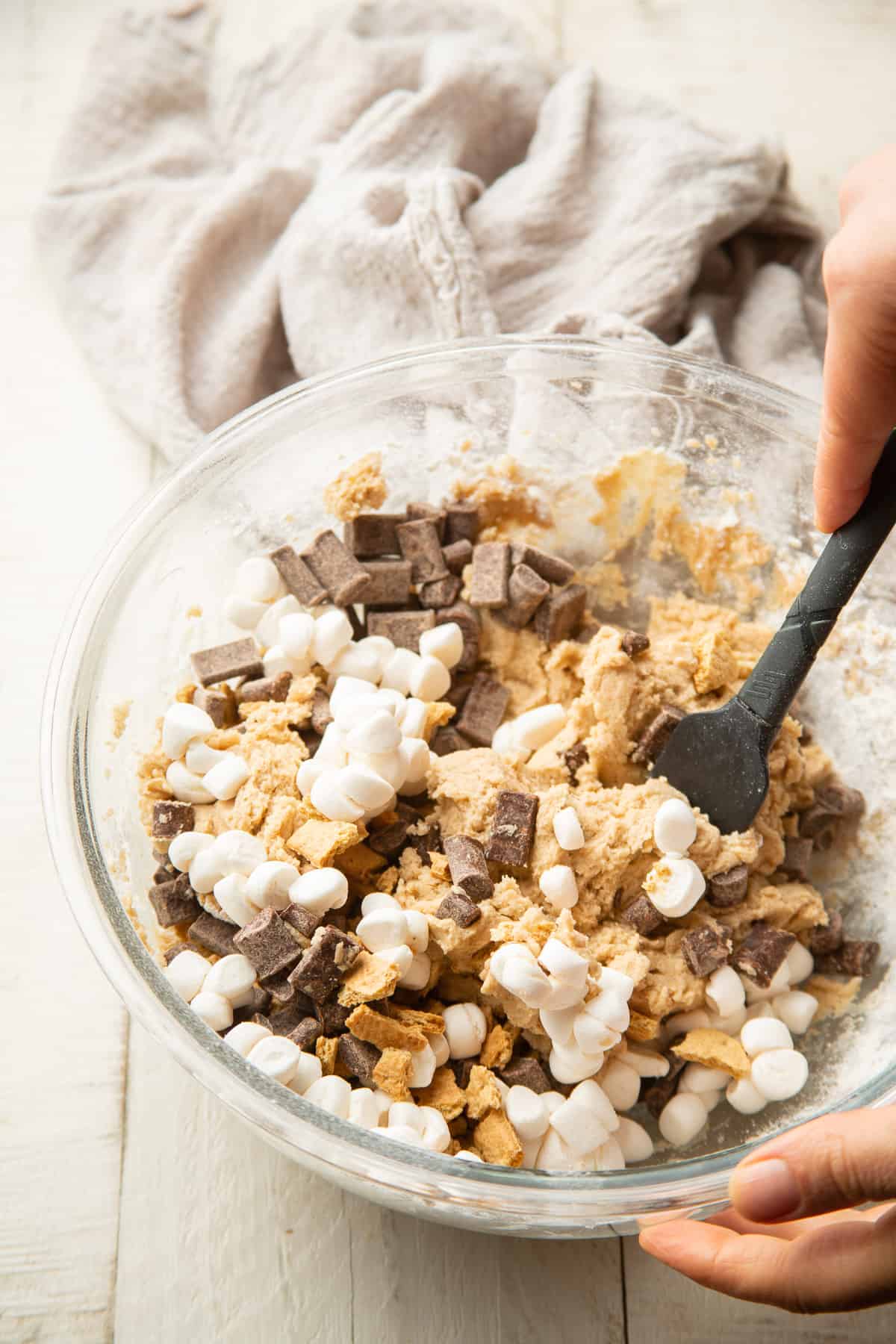 Hand stirring marshmallows, chocolate chips and graham cracker pieces into a bowl of Vegan S'mores Cookie dough.