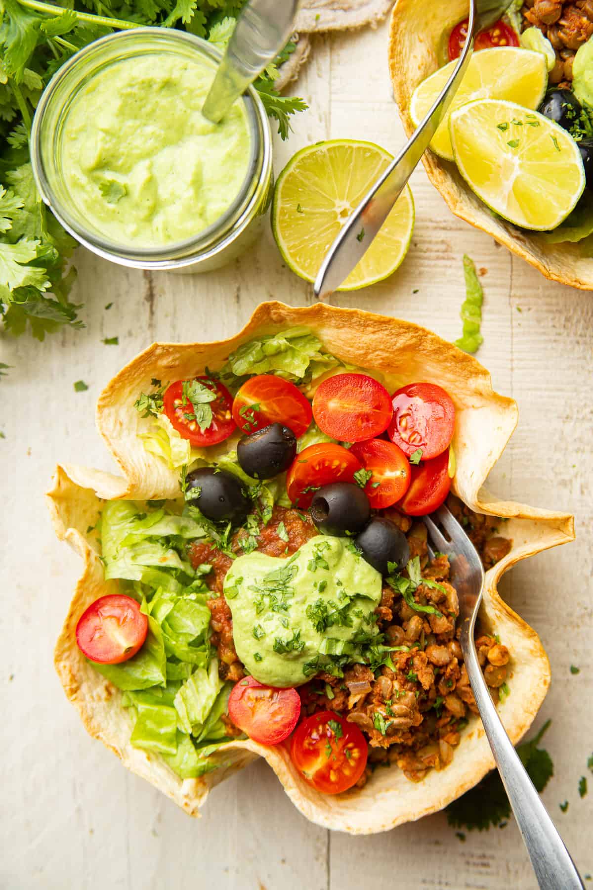 Deux salades tacos végétaliennes et un pot de vinaigrette sur une surface en bois blanche.