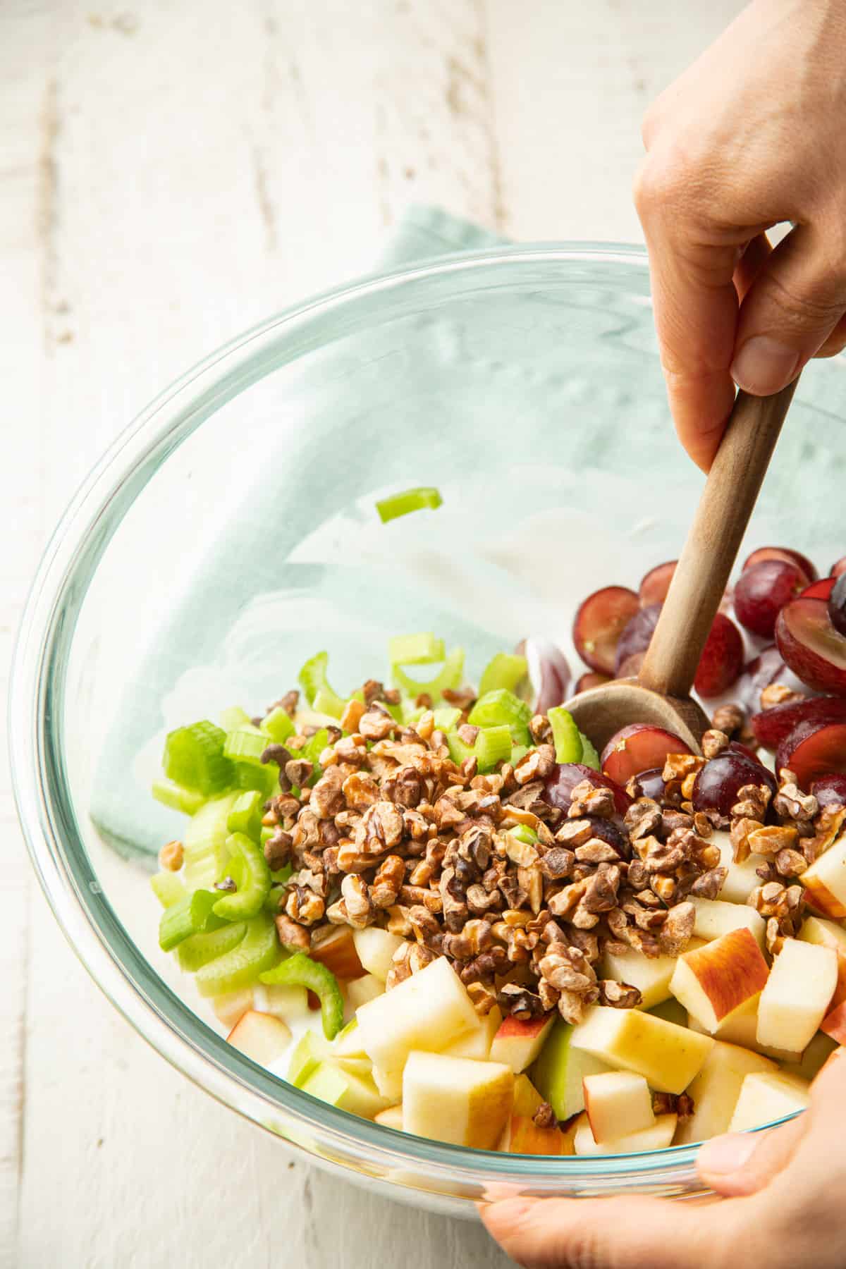 Hand stirring Vegan Waldorf Salad ingredients together in a bowl.