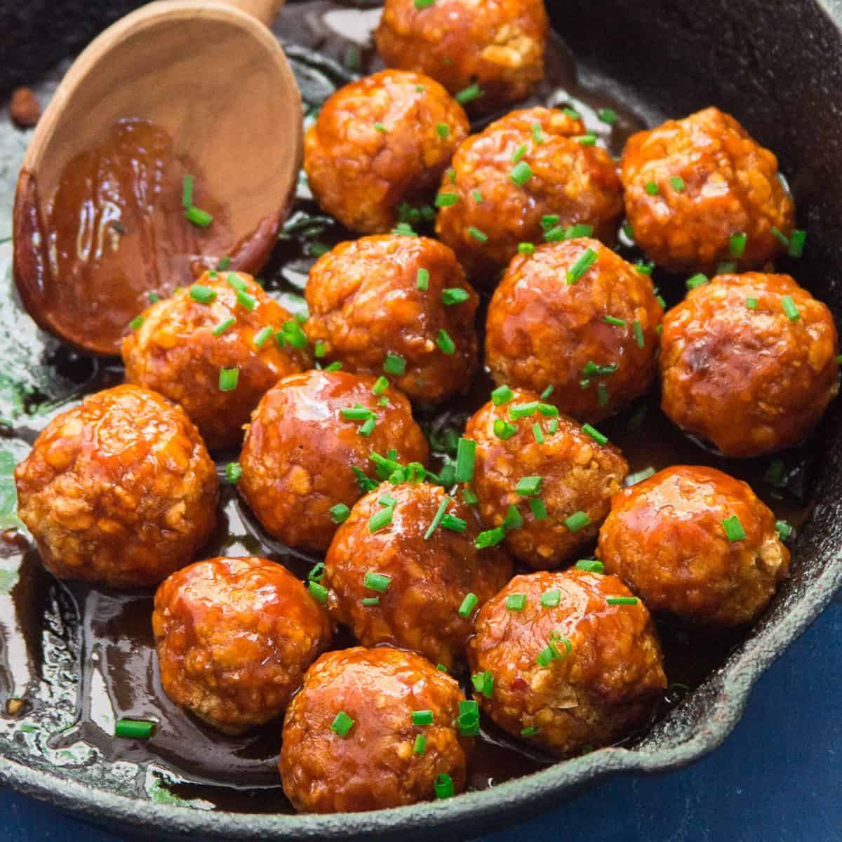 Firecracker Chickpea Meatballs topped with chives in a cast iron skillet.