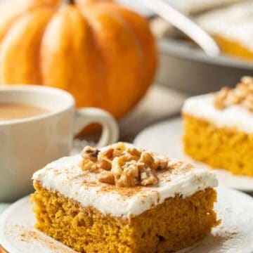 Slice of Vegan Pumpkin Cake on a plate, with pumpkin, coffee cup and more cake in the background.