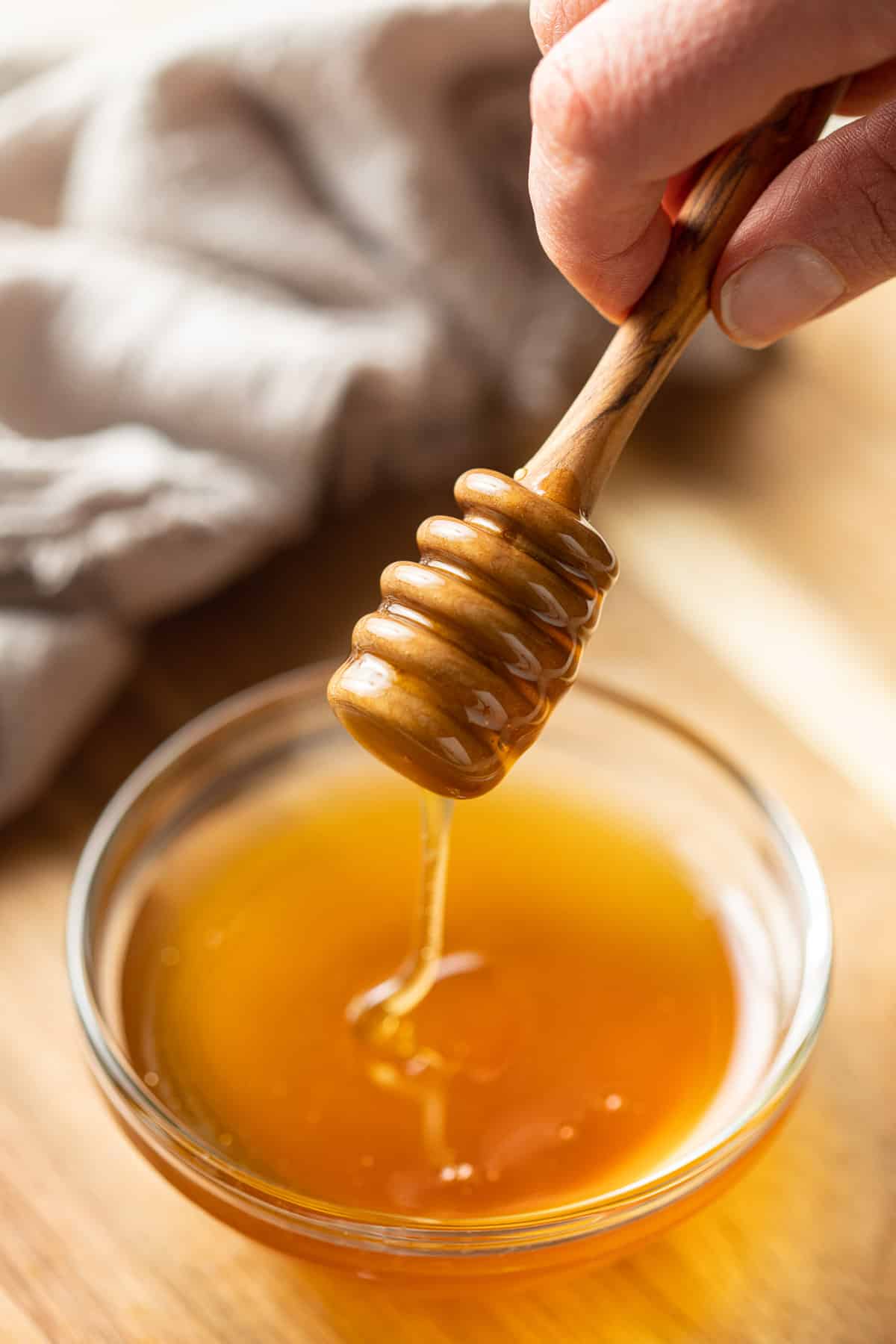 Hand holding a honey dipper drizzling vegan honey into a bowl.