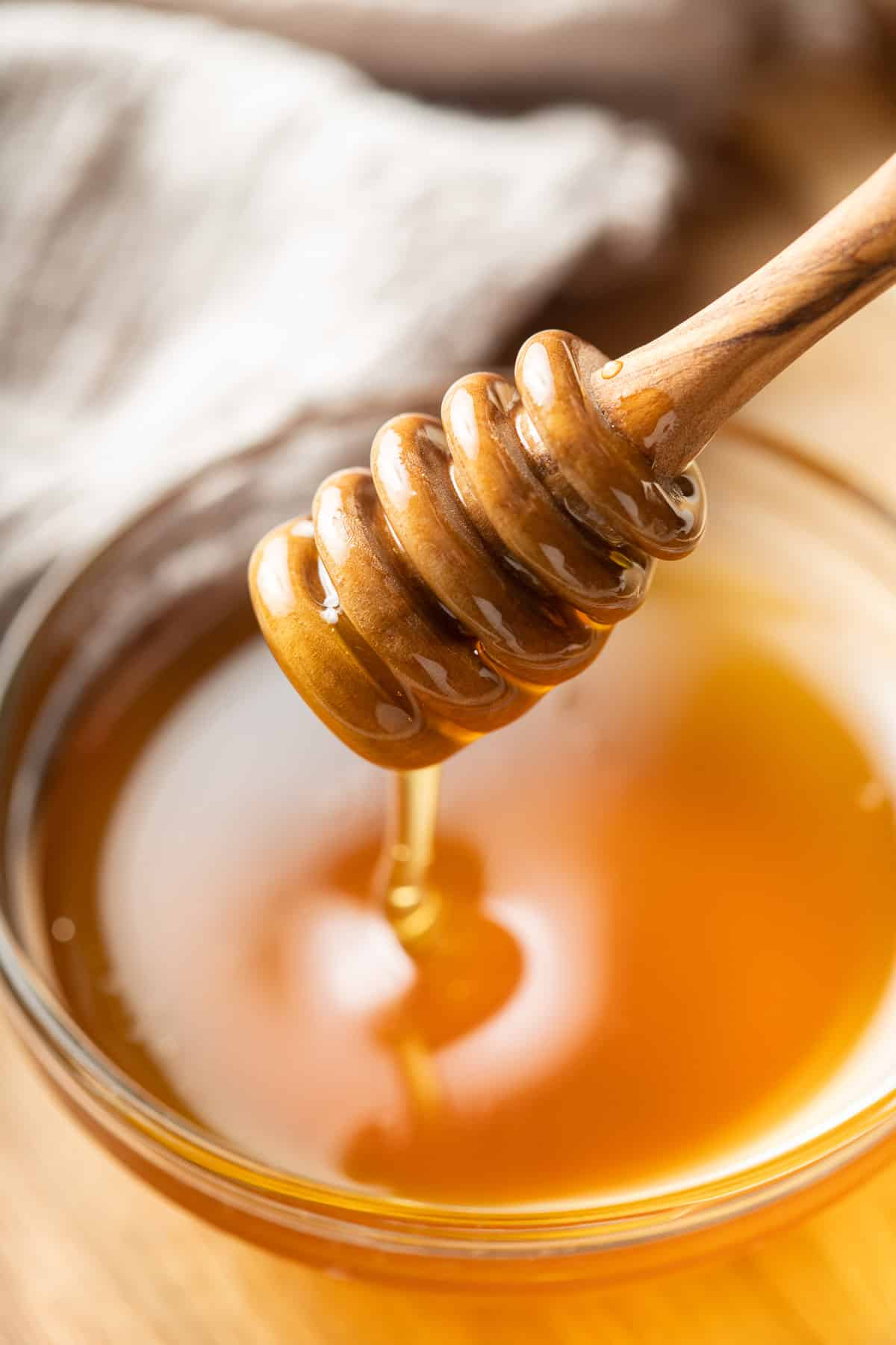 Close up of a honey dipper drizzling vegan honey into a bowl.