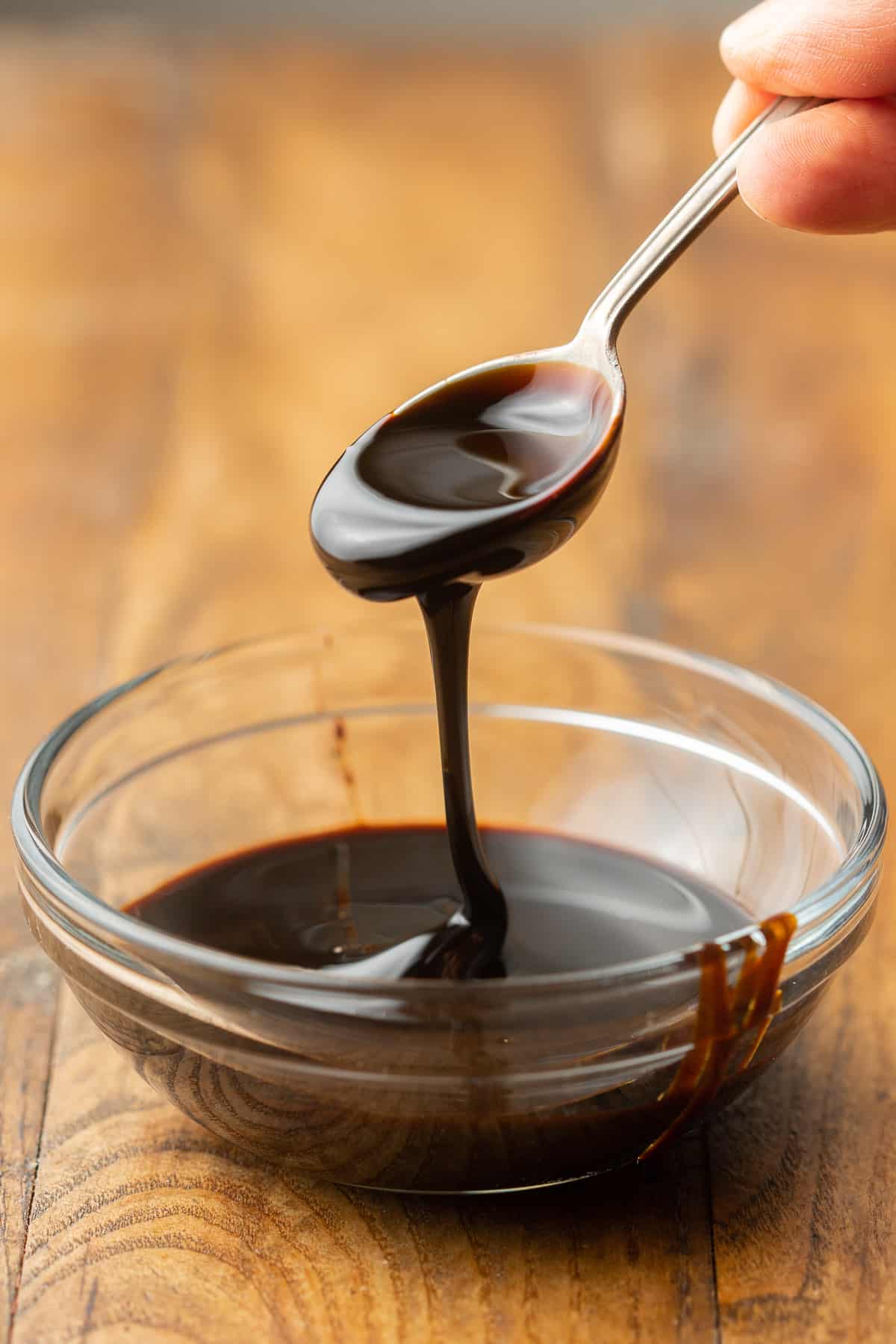 Spoon drizzling blackstrap molasses into a glass bowl.