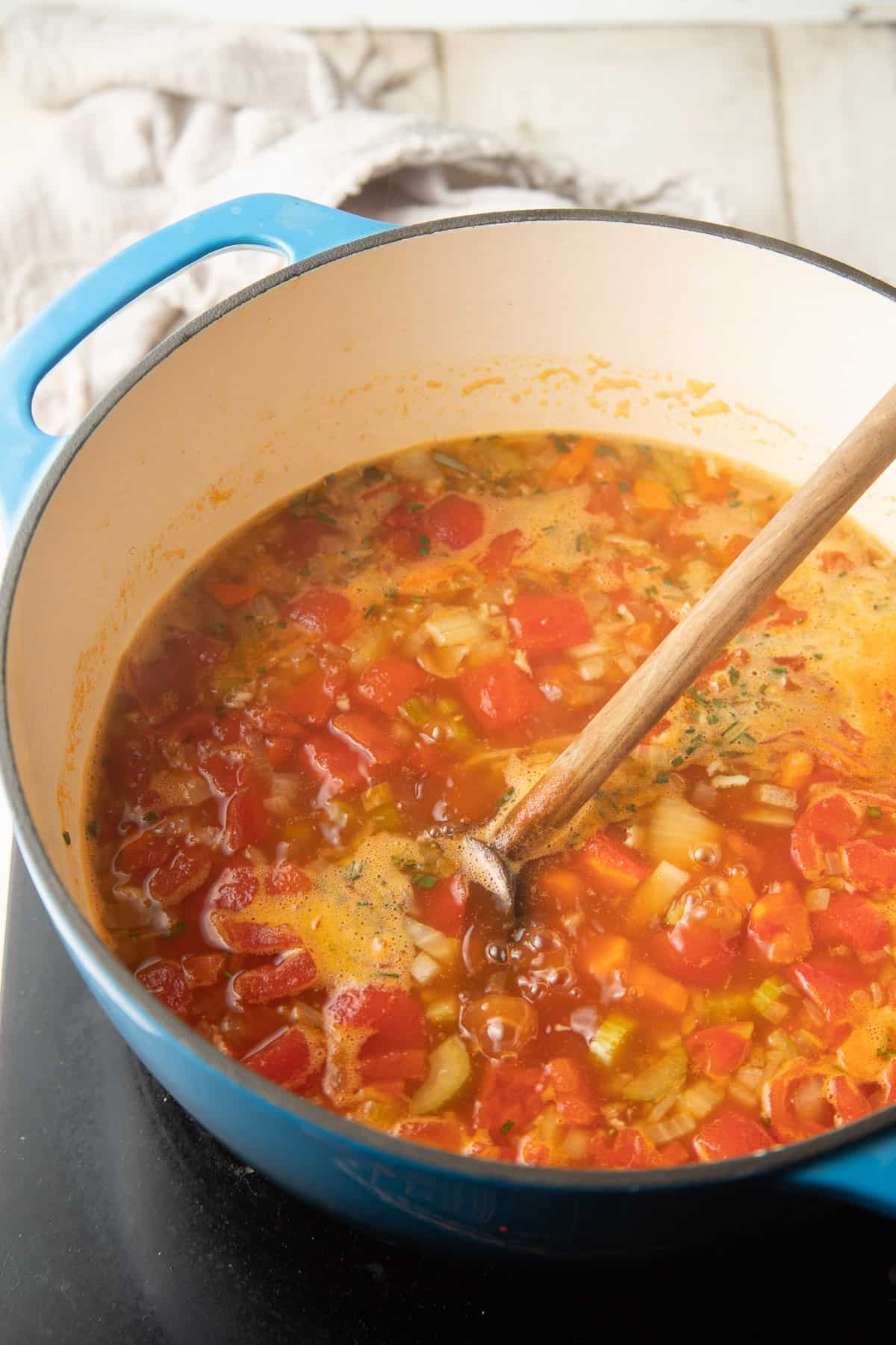 Tomatoes, vegetables, and rosemary simmering in broth in a pot.