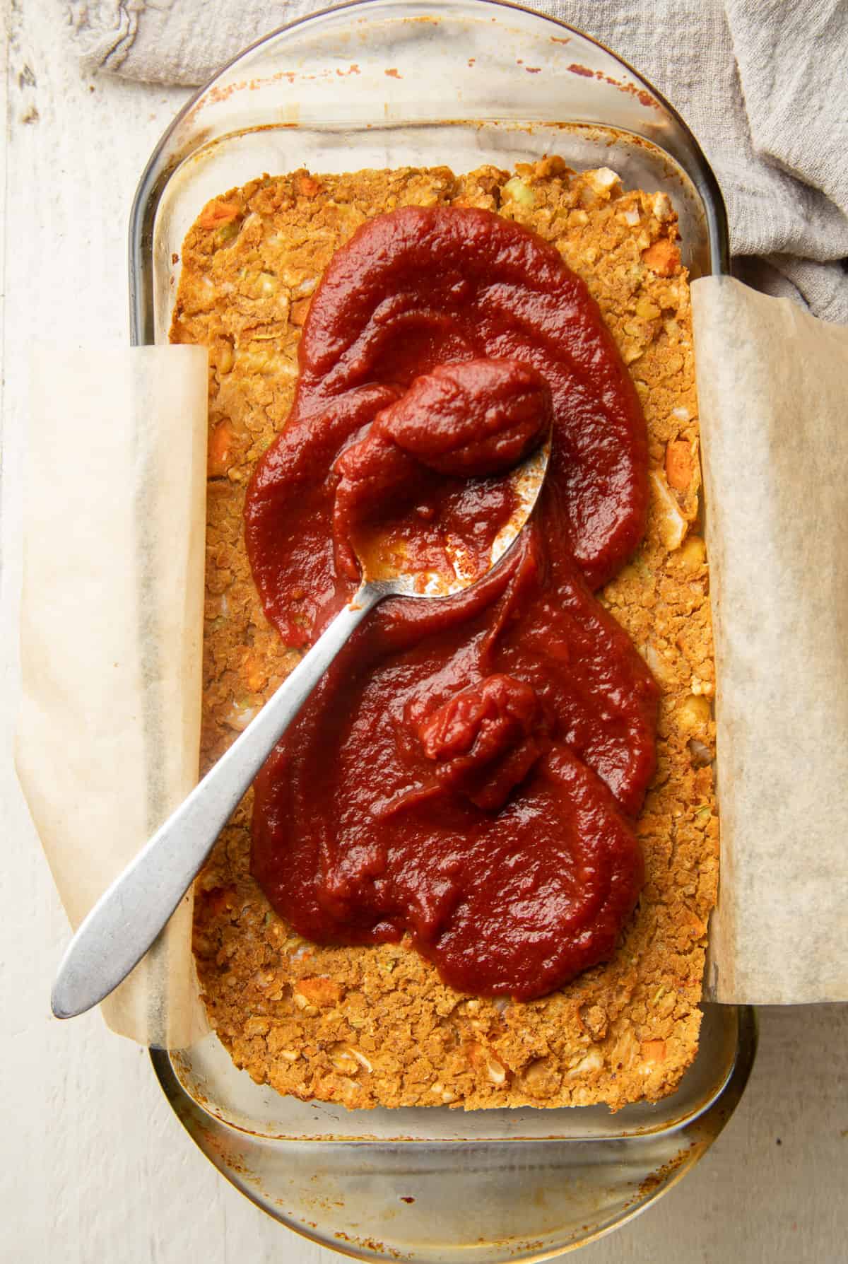 Partially baked Vegan Meatloaf with glaze and spoon on top.