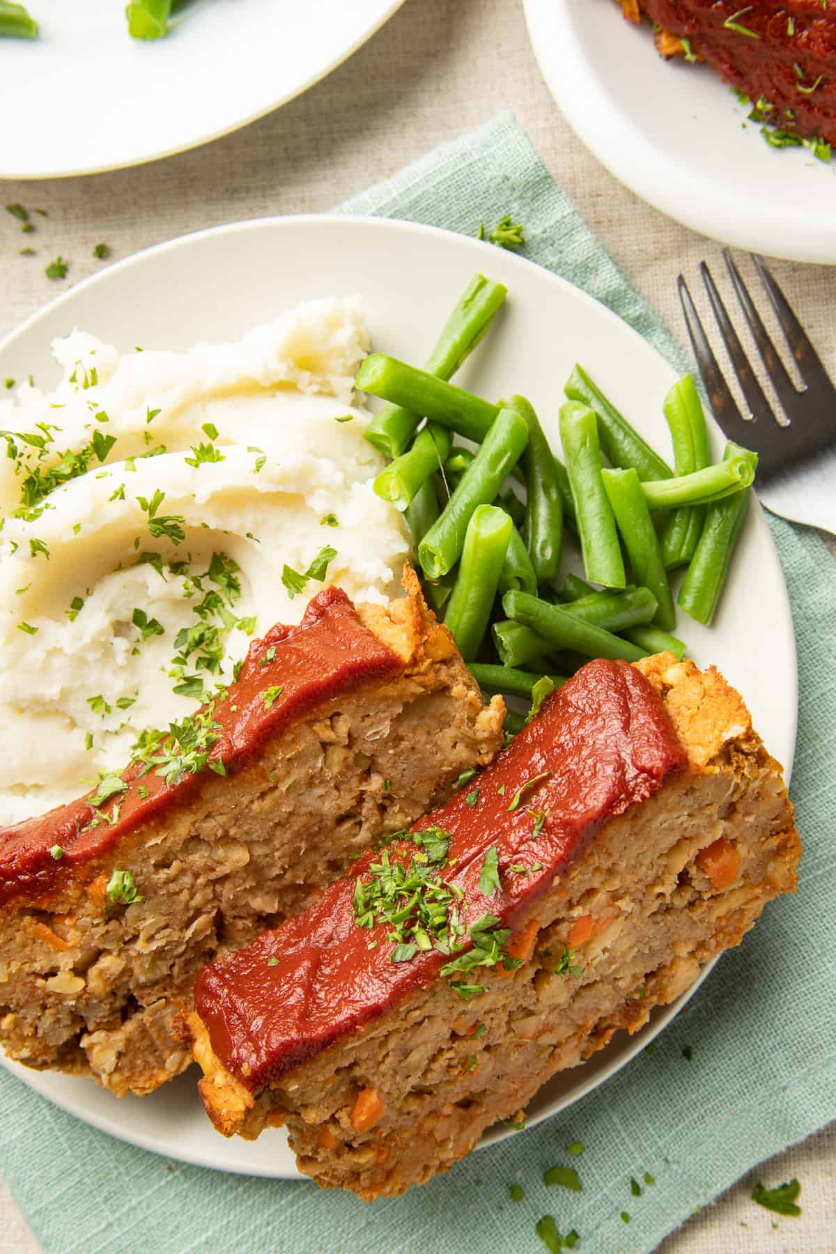 Two slices of Vegan Meatloaf on a plate with mashed potatoes and green beans.