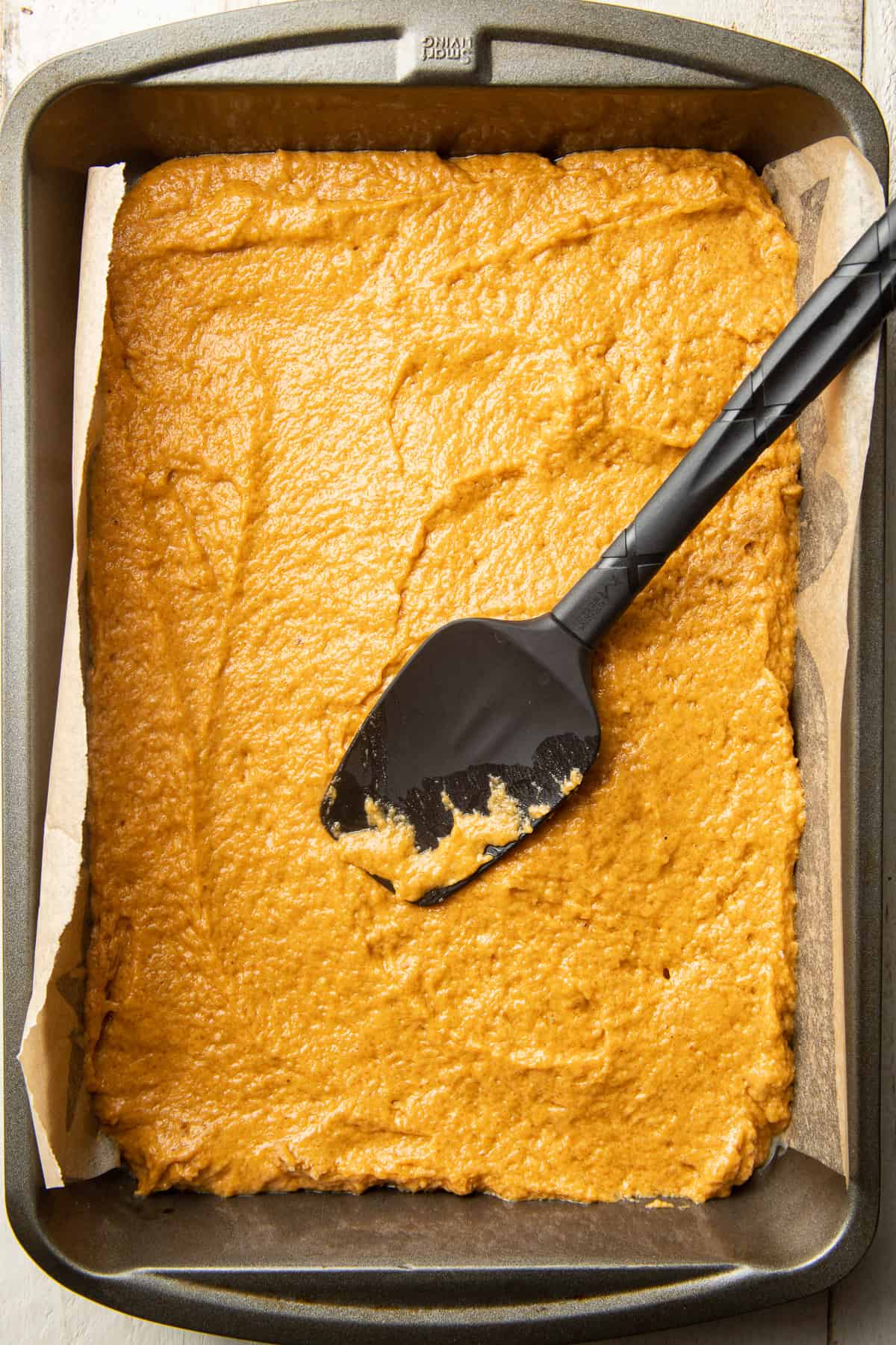 Pumpkin cake batter in a baking pan with a spatula on top.