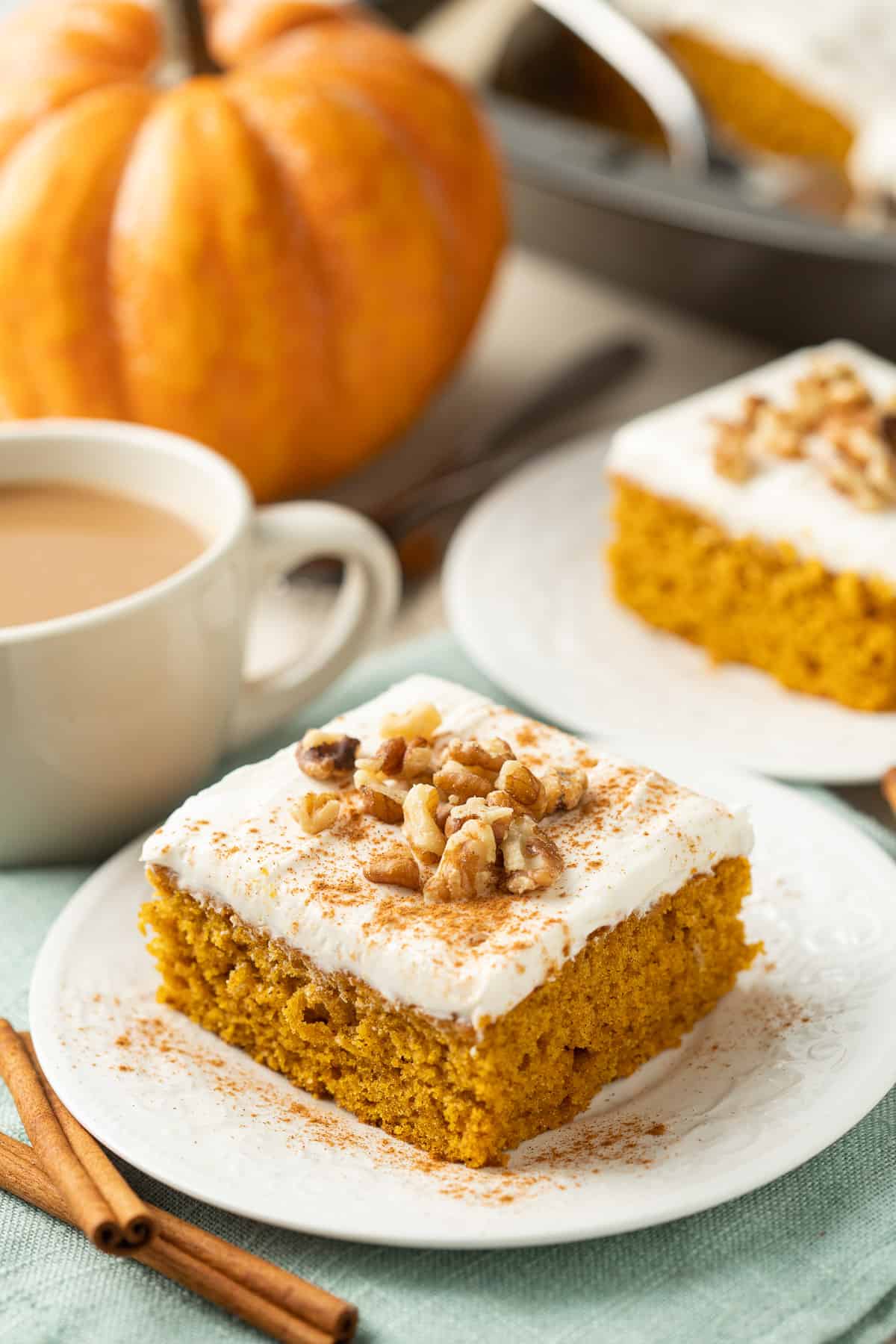 Two slices of Vegan Pumpkin Cake on dishes, pumpkin and cup of coffee on a table.