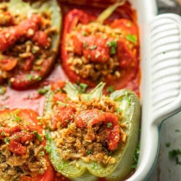 Vegan Stuffed Peppers in a baking dish with tomato sauce and vegan Parmesan cheese.