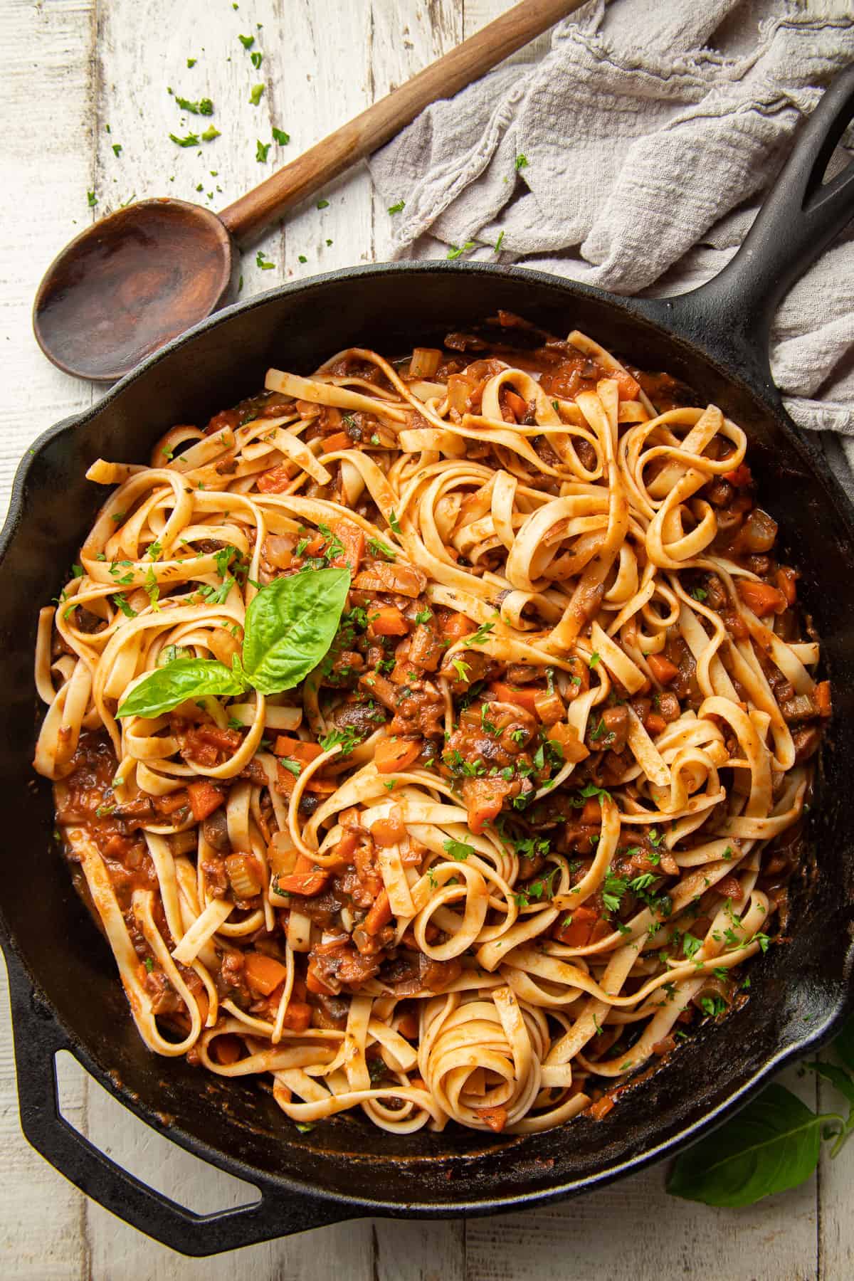 Skillet full of pasta with Mushroom Bolognese on a white wooden surface.