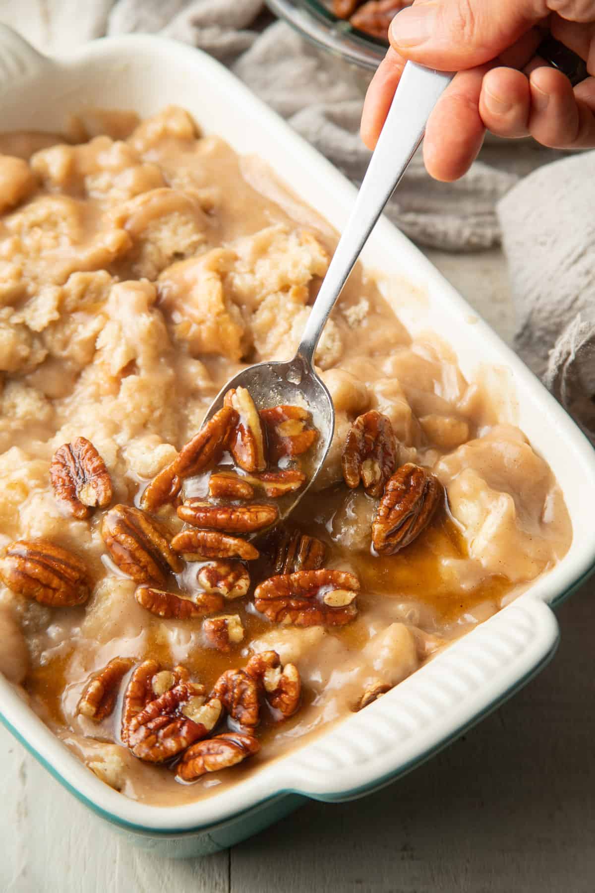Hand spooning pecan topping over unbaked Vegan Bread Pudding.