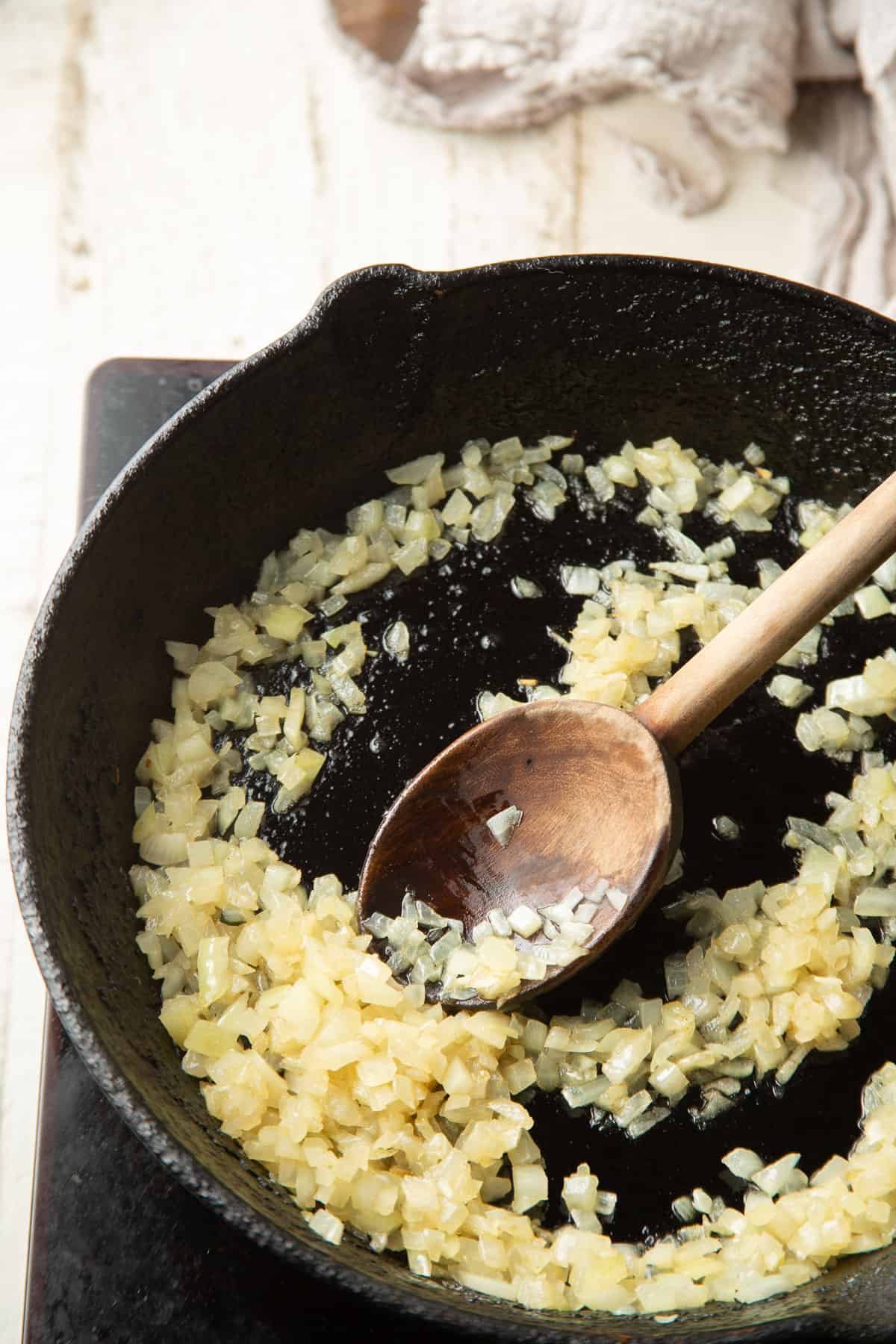 Onions cooking in a skillet with a wooden spoon.