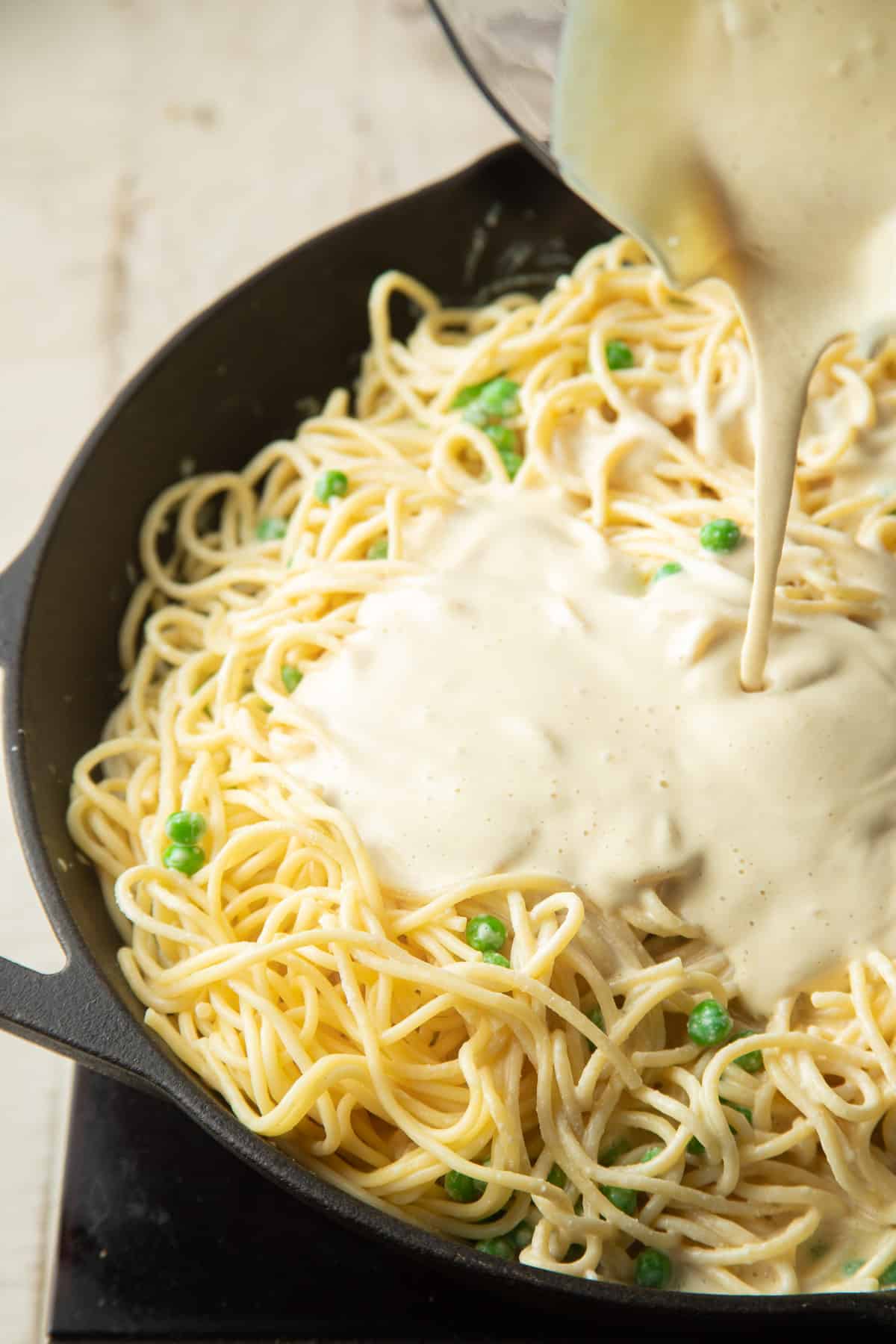 Vegan carbonara sauce being poured over a skillet of spaghetti.