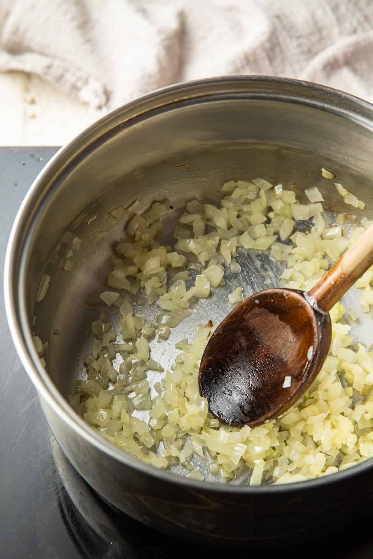 Onions cooking in a saucepan with a wooden spoon.