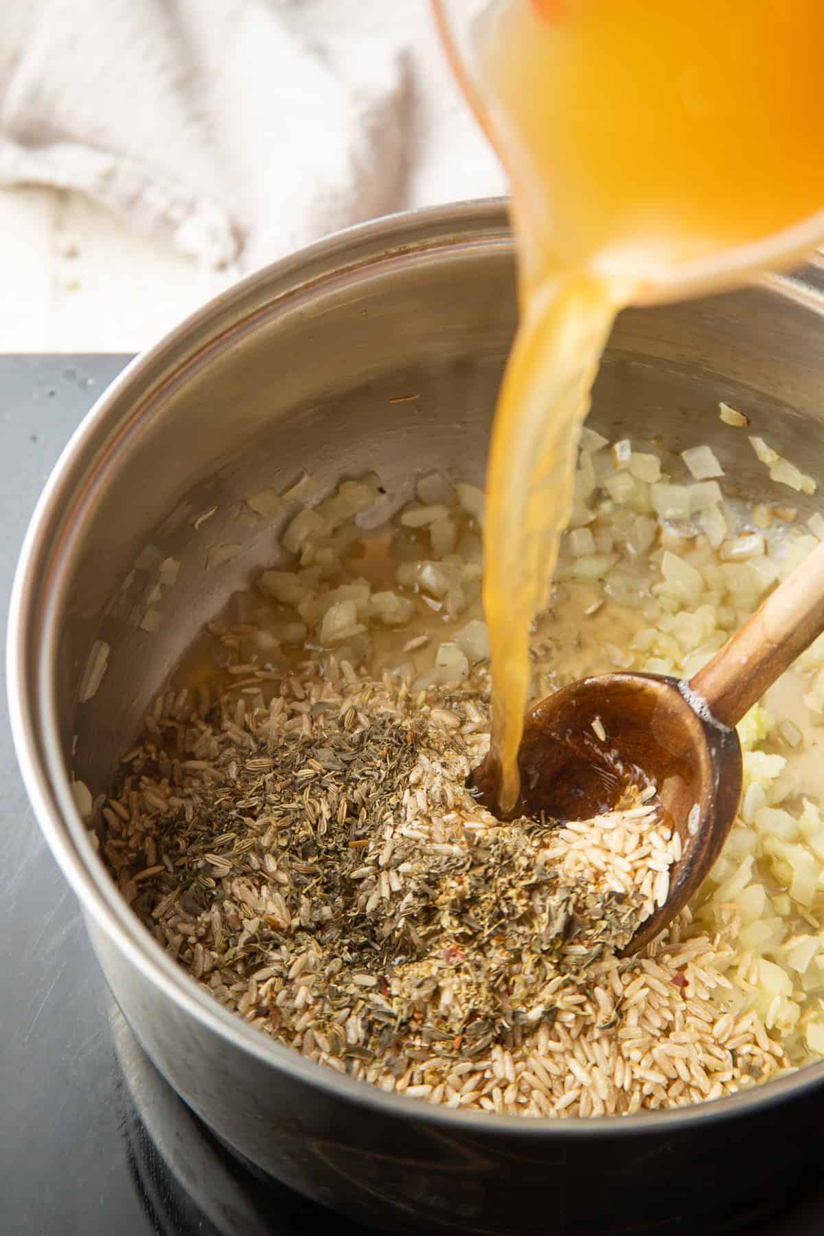 Broth being poured into a saucepan with rice, onions and herbs.