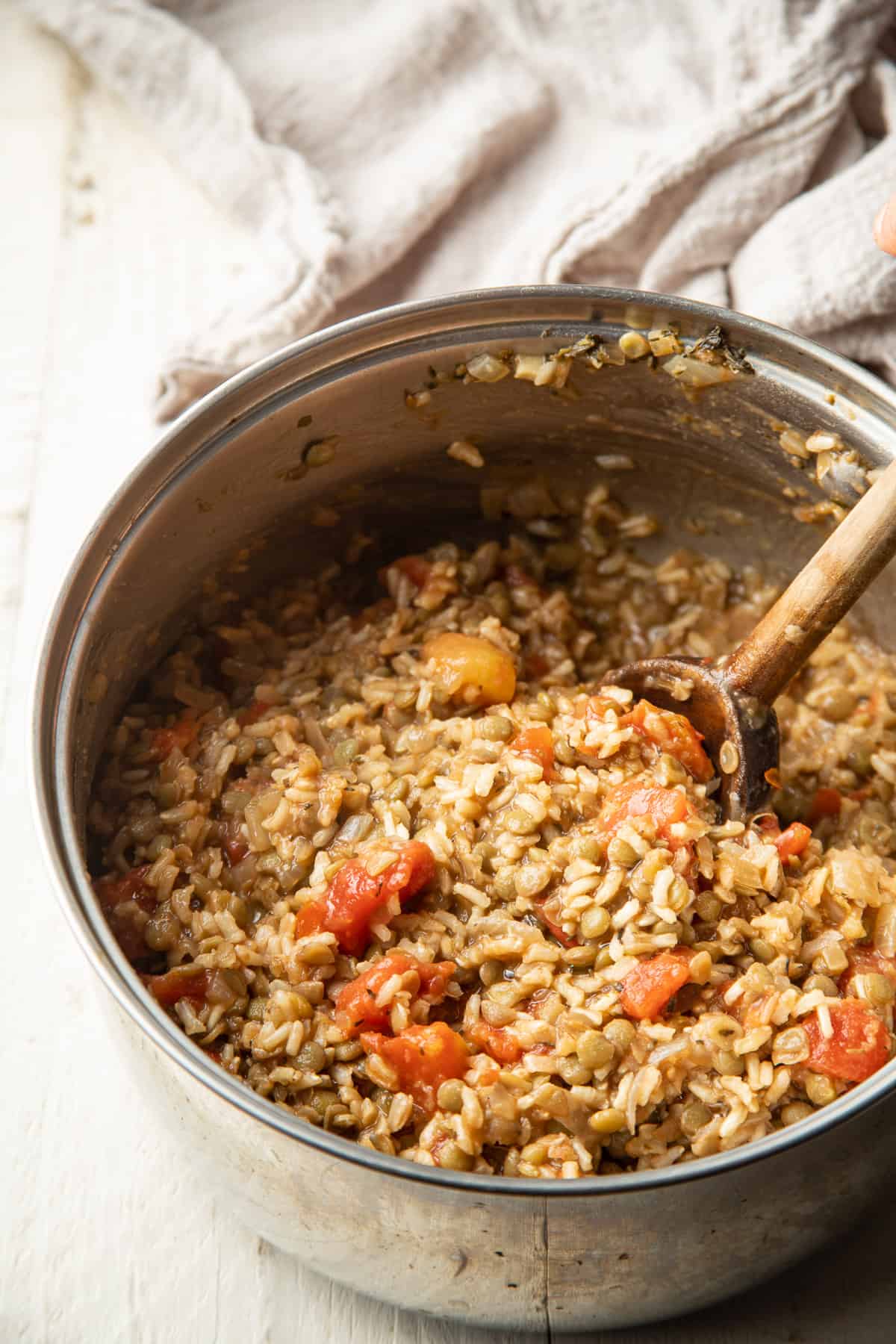 Rice, lentils and tomatoes in a saucepan with wooden spoon.