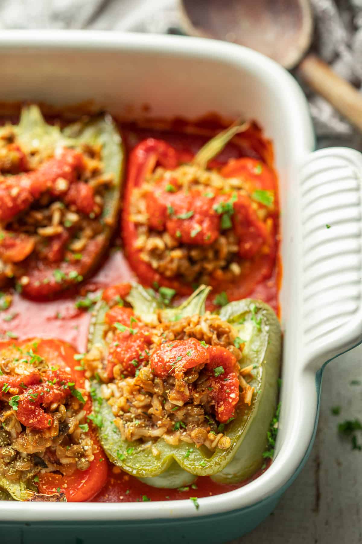 Vegan Stuffed Peppers in a baking dish with tomato sauce and vegan Parmesan cheese.