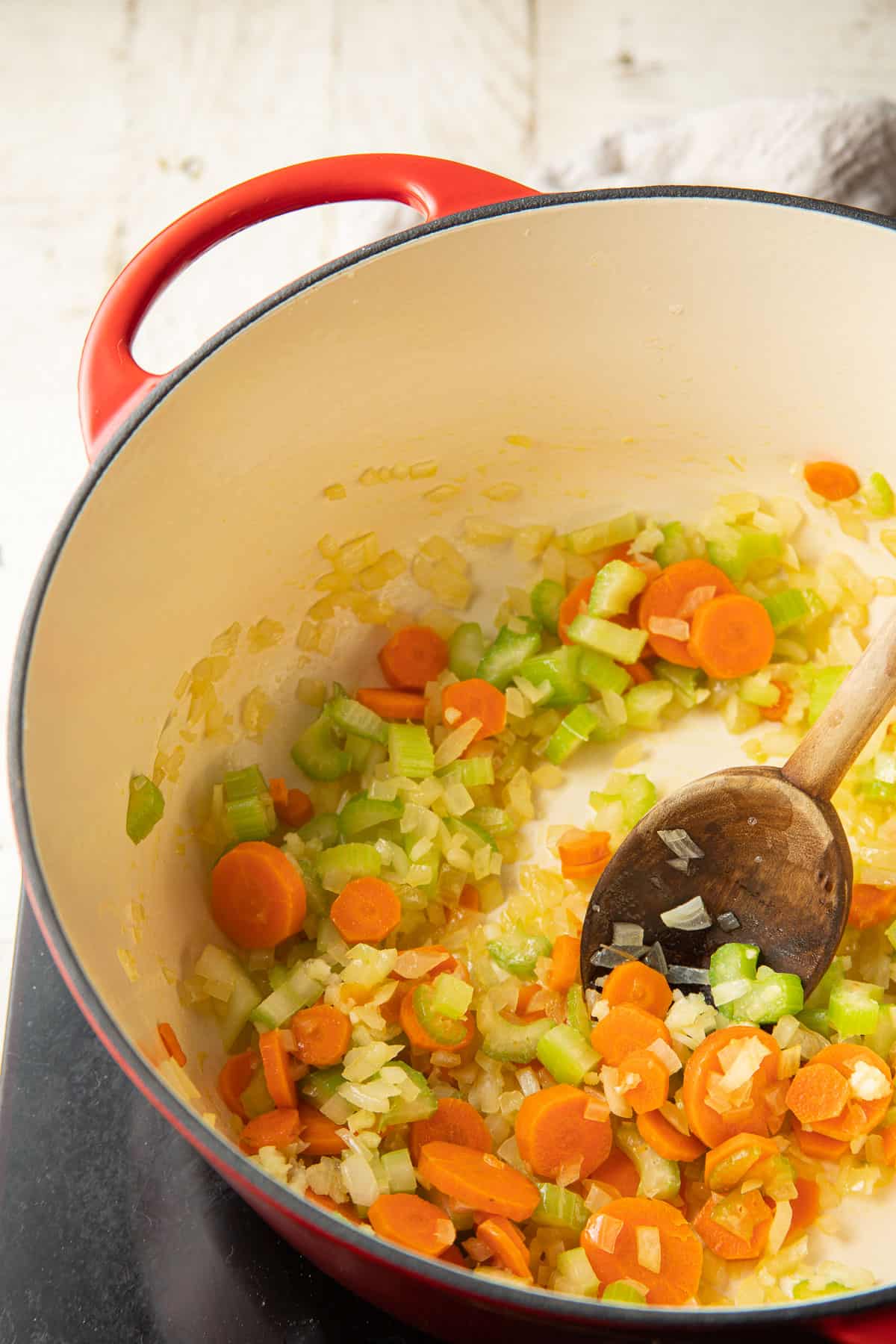 Onions, carrots, and celery cooking in a pot with a wooden spoon.