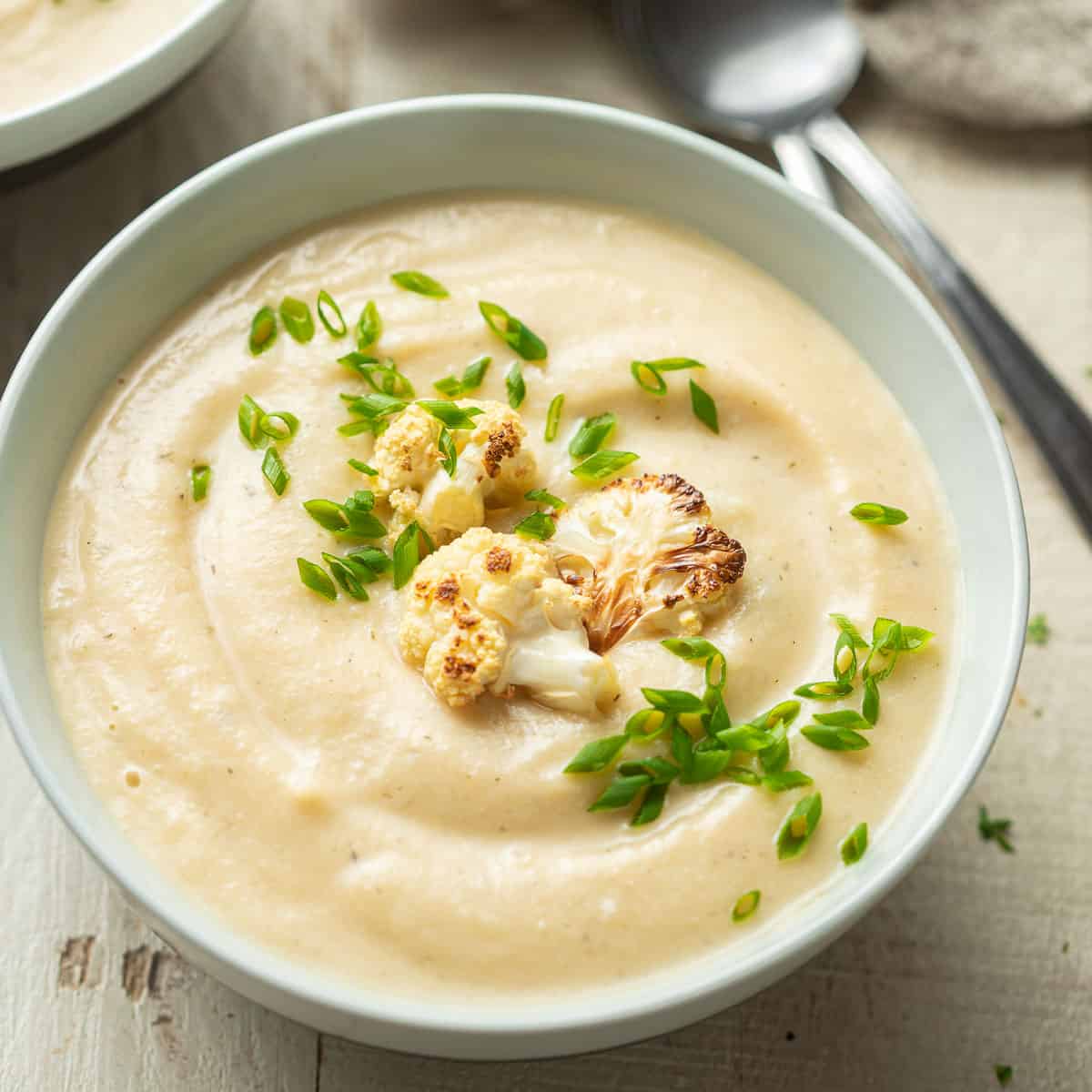 Bowl of Vegan Cauliflower Soup with chives and roasted cauliflower florets on top.