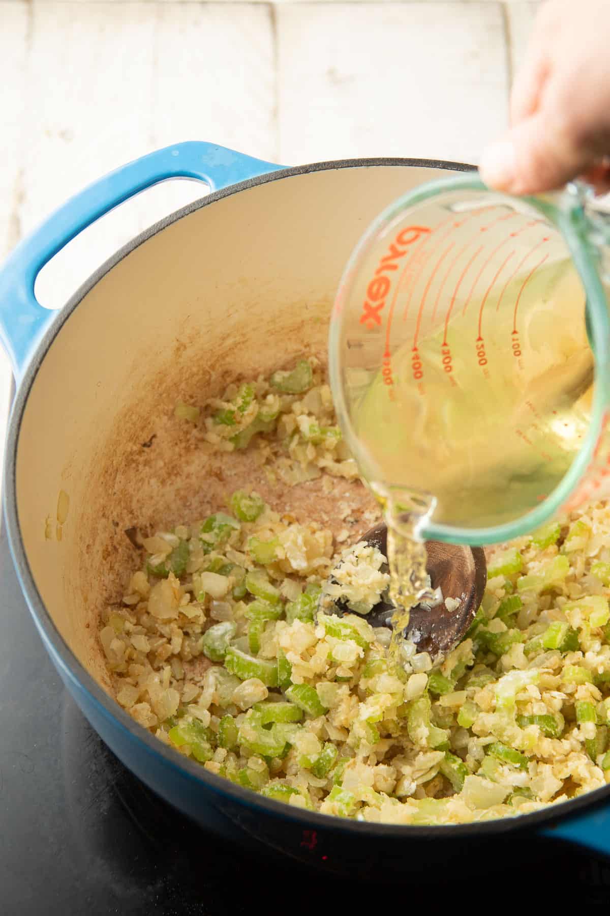 Hand pouring wine into a pot of celery, onions, and flour.