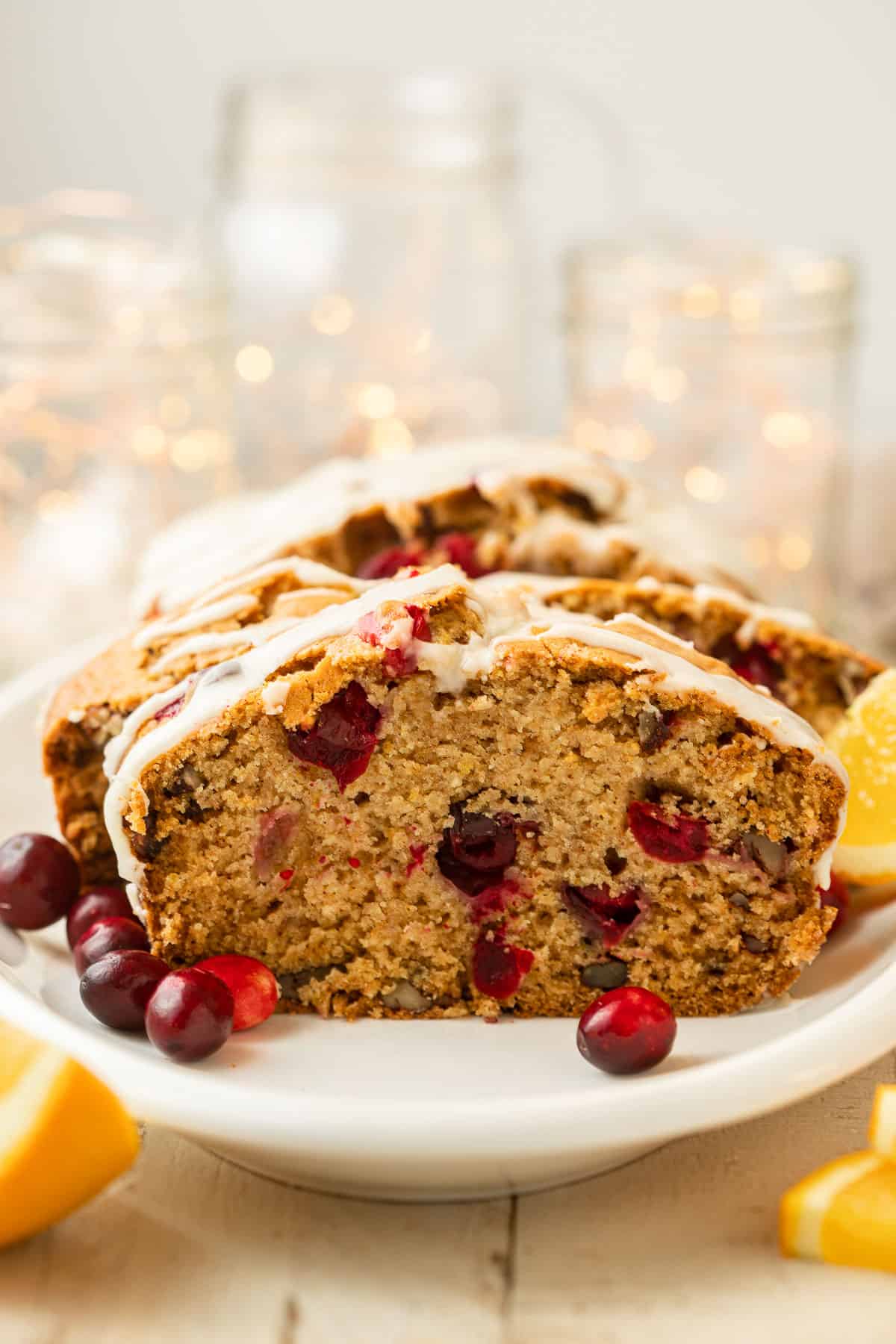 Sliced loaf of Vegan Cranberry Bread on a dish with twinkle lights in the background.