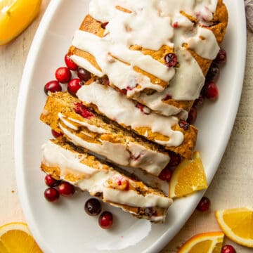 Overhead view of a sliced loaf of Vegan Cranberry Bread with orange slices and fresh cranberries.