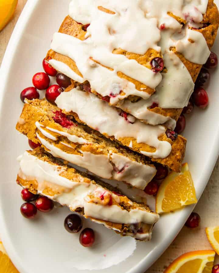 Overhead view of a sliced loaf of Vegan Cranberry Bread with orange slices and fresh cranberries.