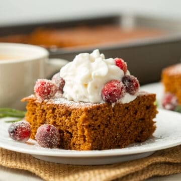 Slice of Vegan Gingerbread Cake on a plate with whipped cream and sugared cranberries.