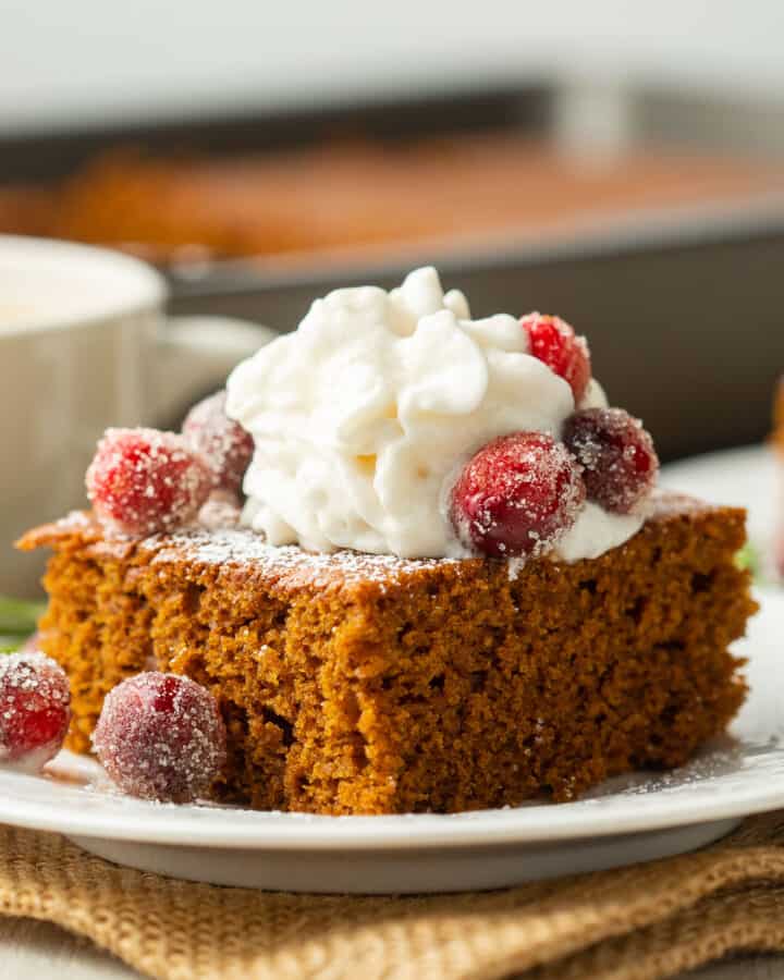 Slice of Vegan Gingerbread Cake on a plate with whipped cream and sugared cranberries.
