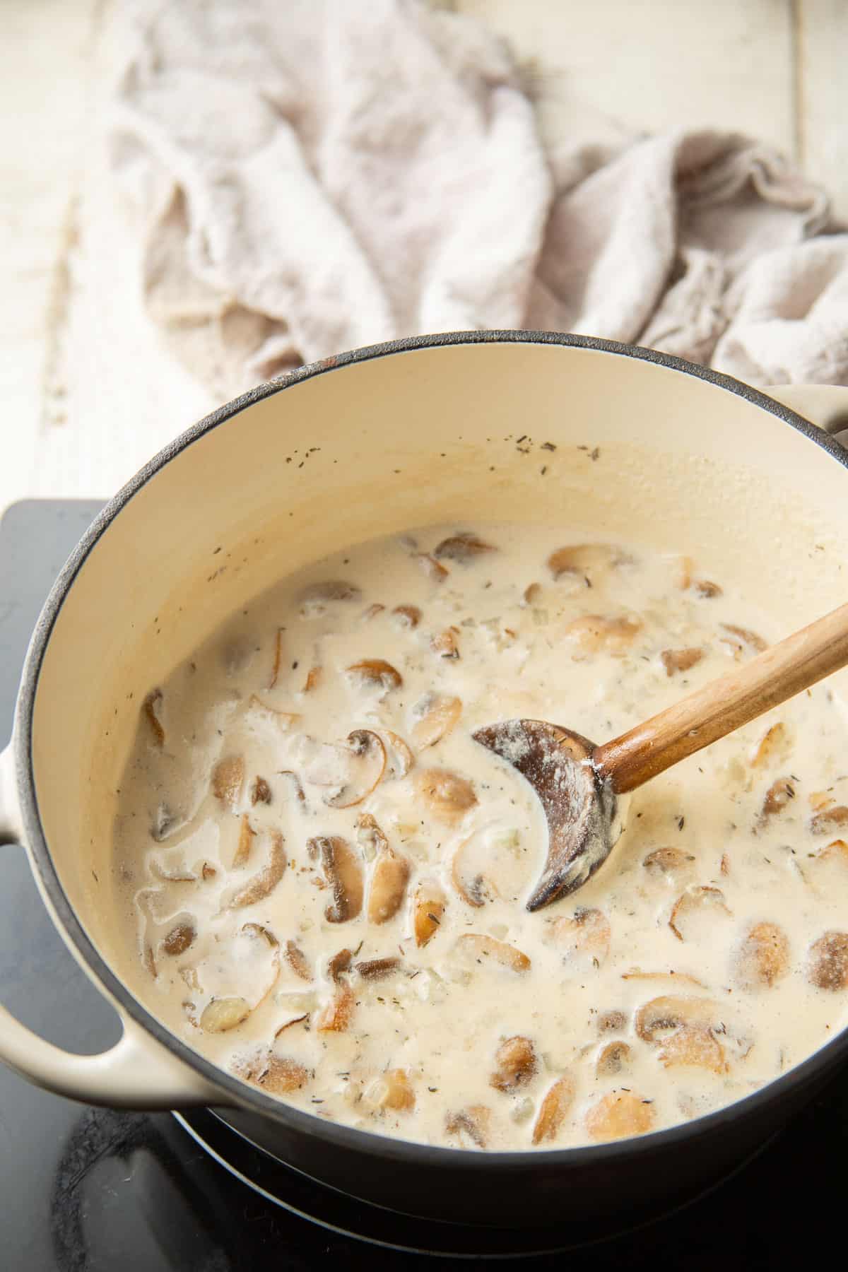 Creamy mushroom sauce cooking in a pot with wooden spoon.