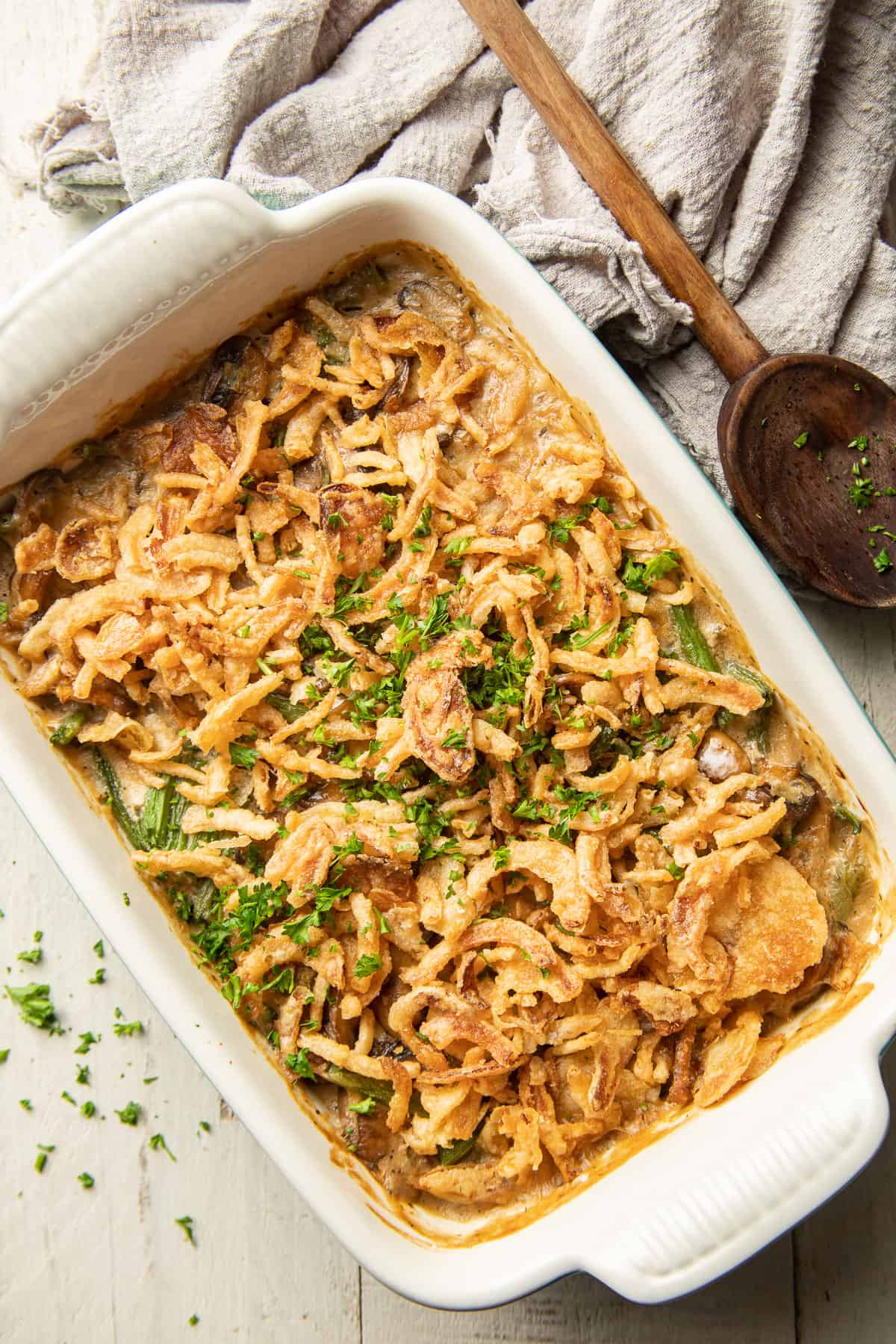 Dish of Vegan Green Bean Casserole on a white wooden surface with wooden spoon on the side.