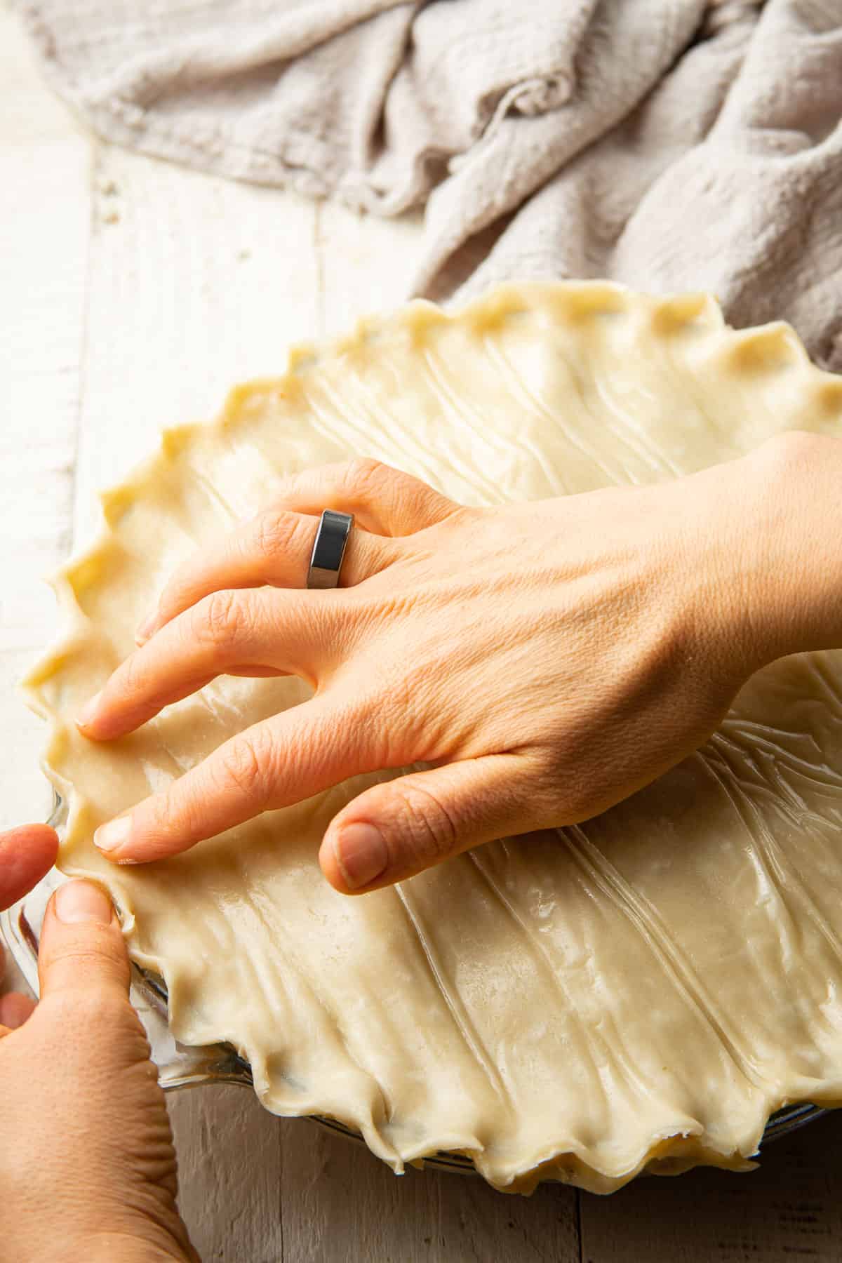 Hands crimping a pie crust on a pot pie.