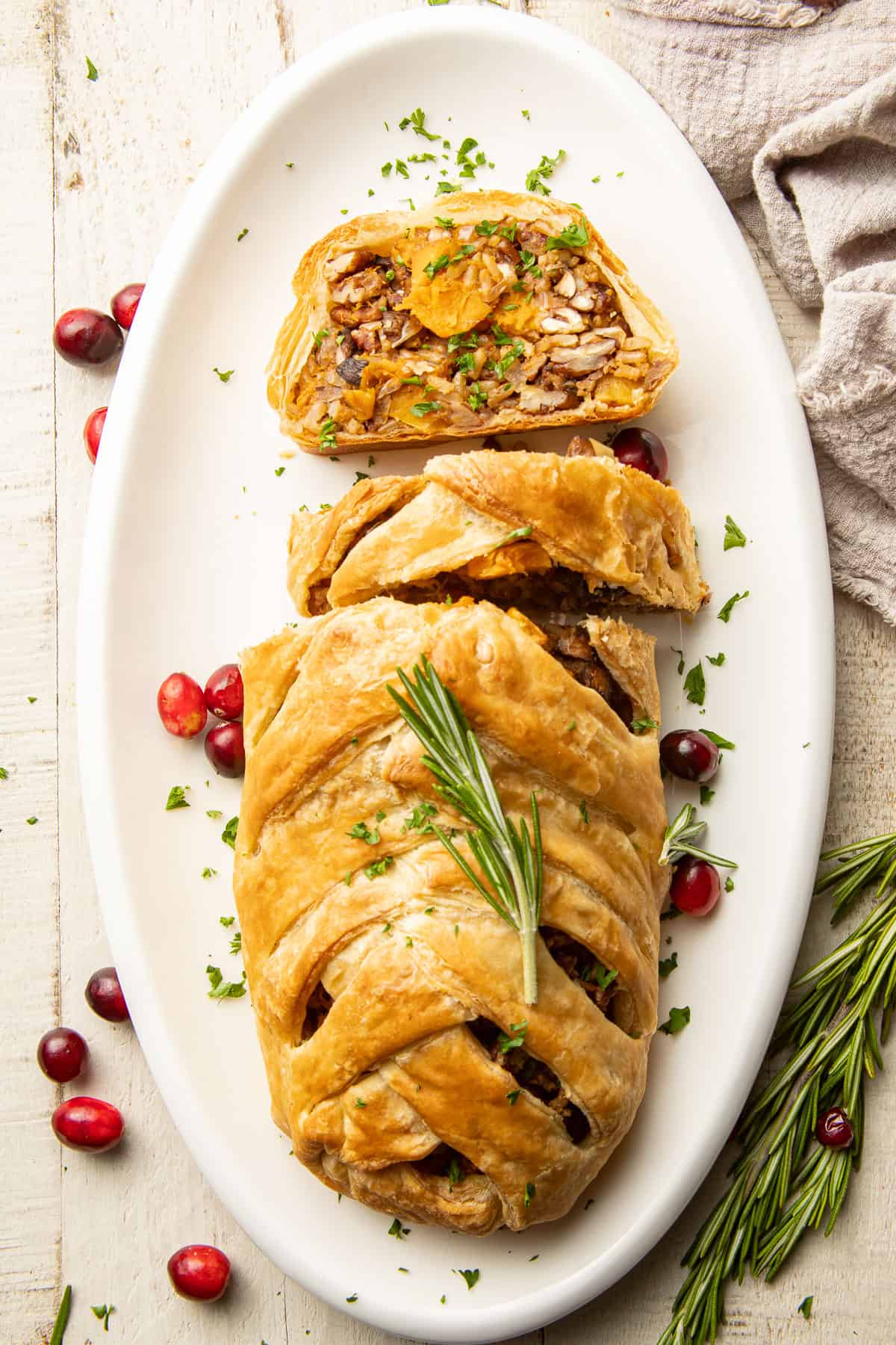 Partially sliced Vegetable Wellington on a serving dish with cranberries and rosemary.
