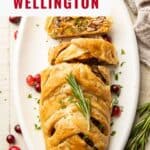 Partially sliced Vegetable Wellington on a serving dish with rosemary and cranberries.