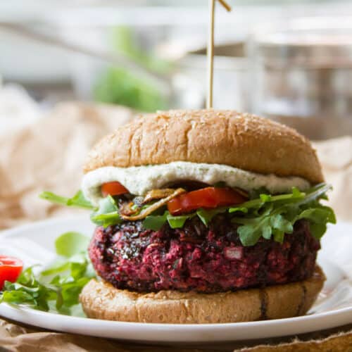 Beet burger topped with greens, tomatoes, and cashew cheese on a bun.