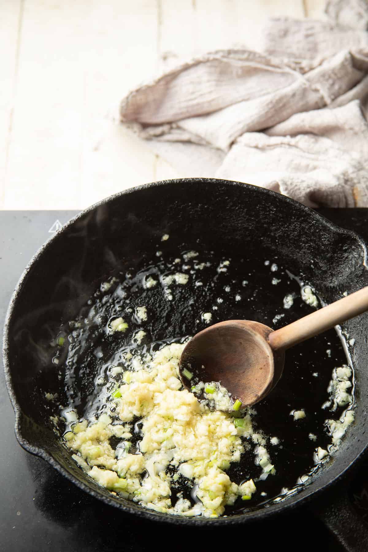 Minced garlic and grated ginger cooking in a skillet with wooden spoon.