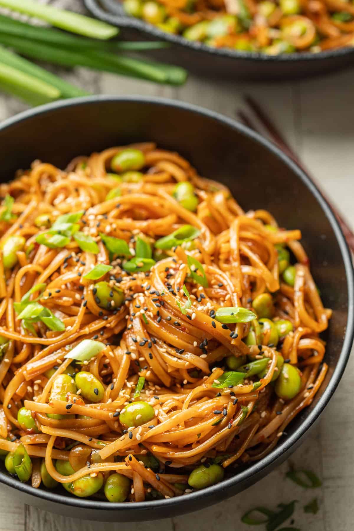 Close up of Chili Garlic Noodles in a bowl with edamame, scallions, and sesame seeds.