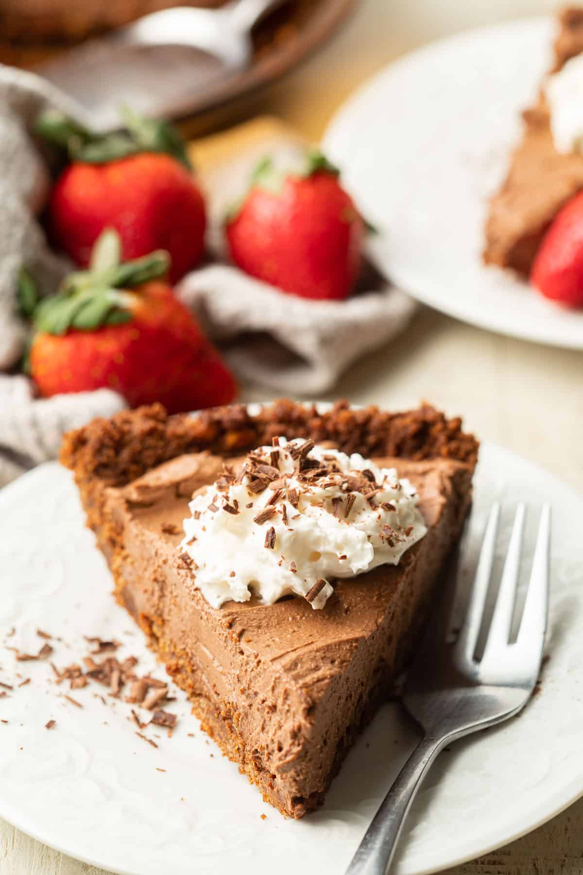 Slice of Vegan Chocolate Pie on a plate with strawberries in the background.