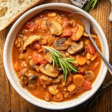 Bowl of Mushroom Stew with a spoon and sprig of rosemary on top.