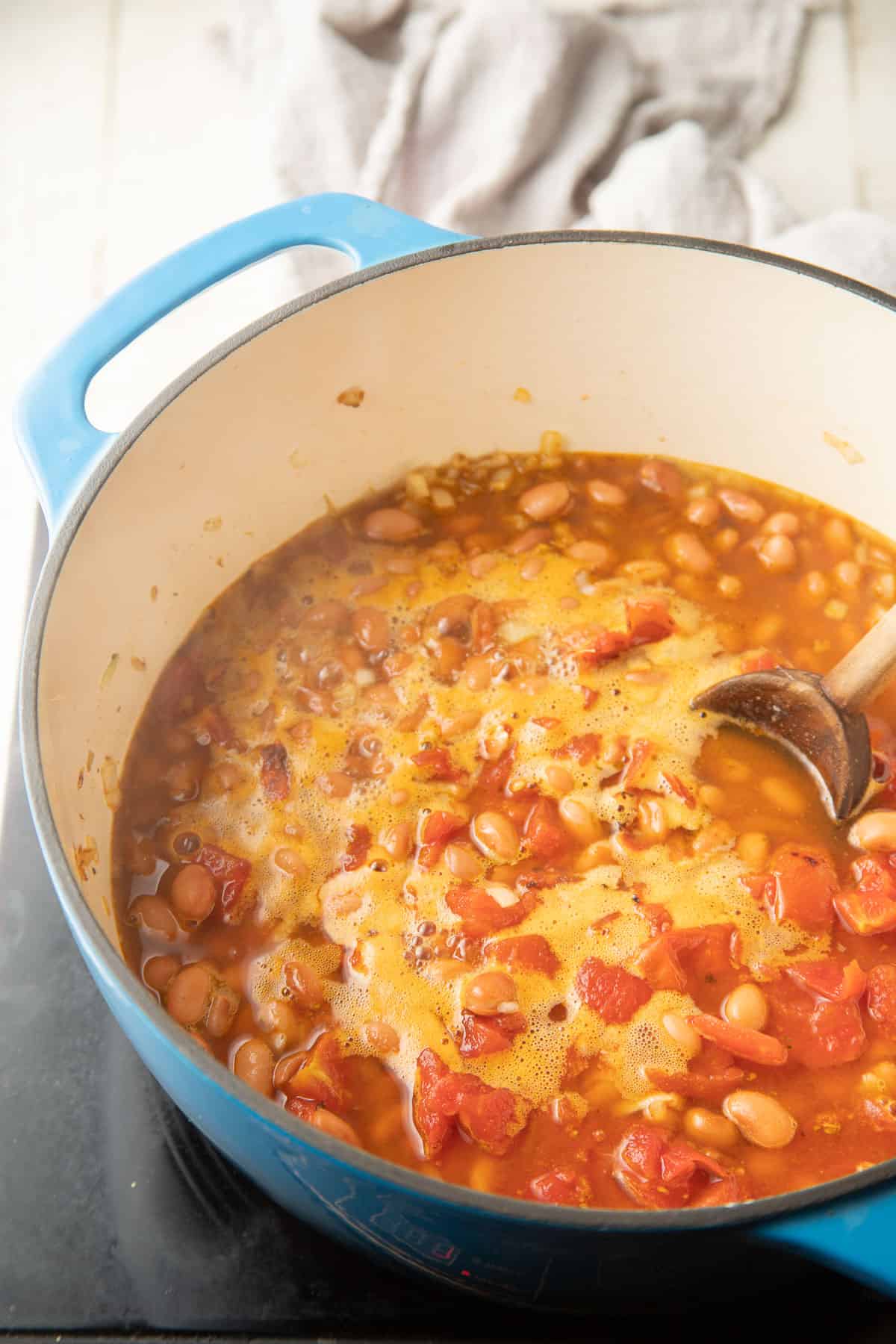 Pinto beans and tomatoes simmering in seasoned broth in a pot.