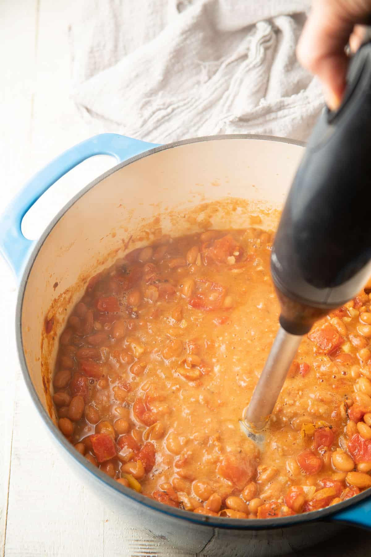 Hand using an immersion blender to blend Pinto Bean Soup in a pot.