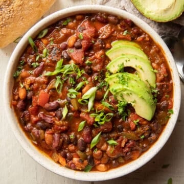 Bowl of vegetarian chili with scallions and avocado slices on top.