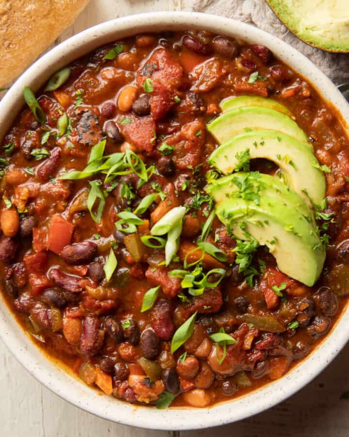 Bowl of vegetarian chili with scallions and avocado slices on top.