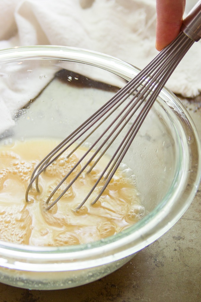 Hand whisking tofu feta marinade together in a glass bowl.