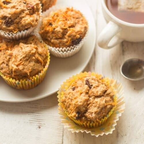 Vegan carrot muffin with plate of muffins and tea cup in the background.