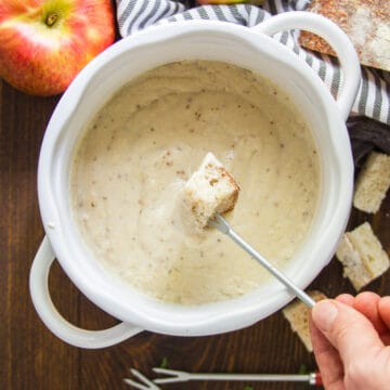 Hand dipping a bread cube on a fork into a pot of vegan fondue.